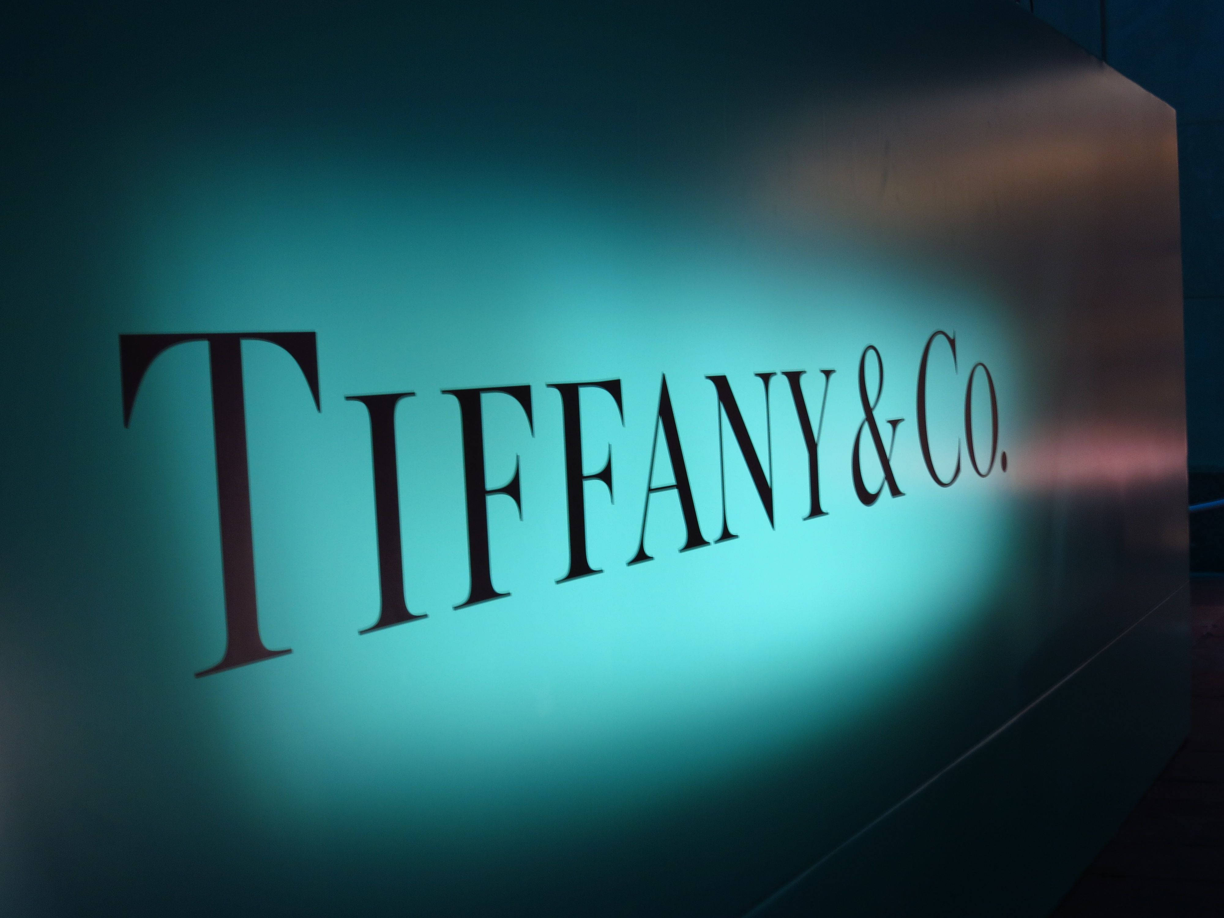 tiffany 桌布 壁紙 — 一個發光的Tiffany & Co.標誌，採用優雅的襯線字體，在深色牆壁上被綠松石色燈光照亮。