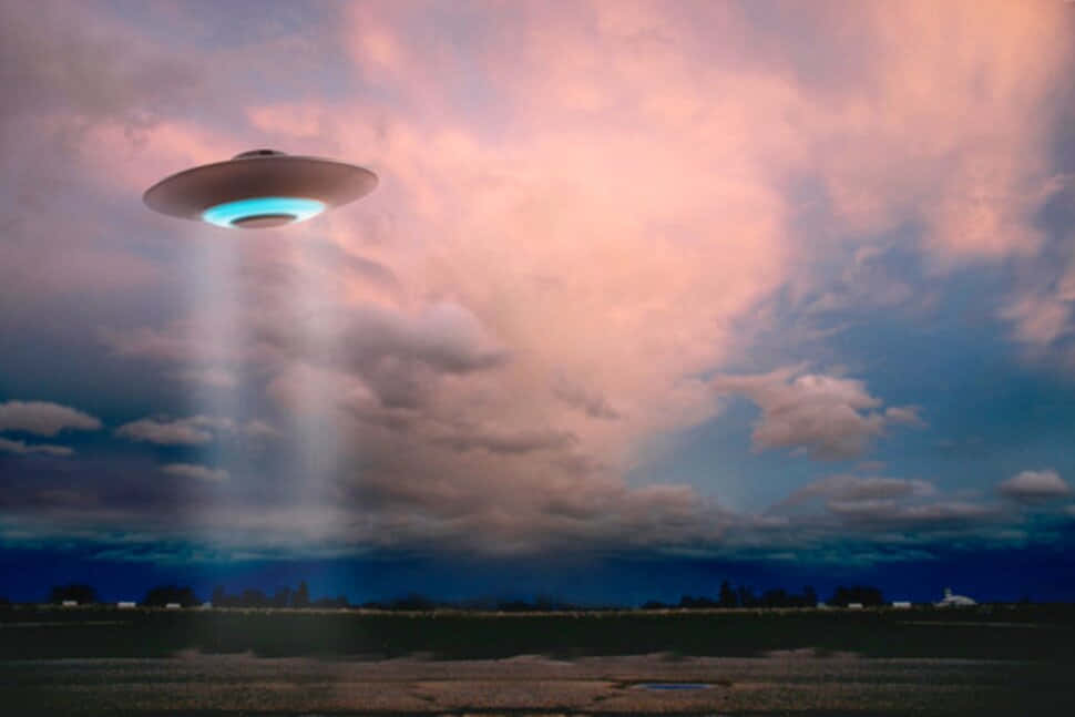 flying 桌布 壁紙 — 一個發光的UFO在黃昏時分盤旋在田野上空，透過粉紅色和藍色的雲層投射出光束。
