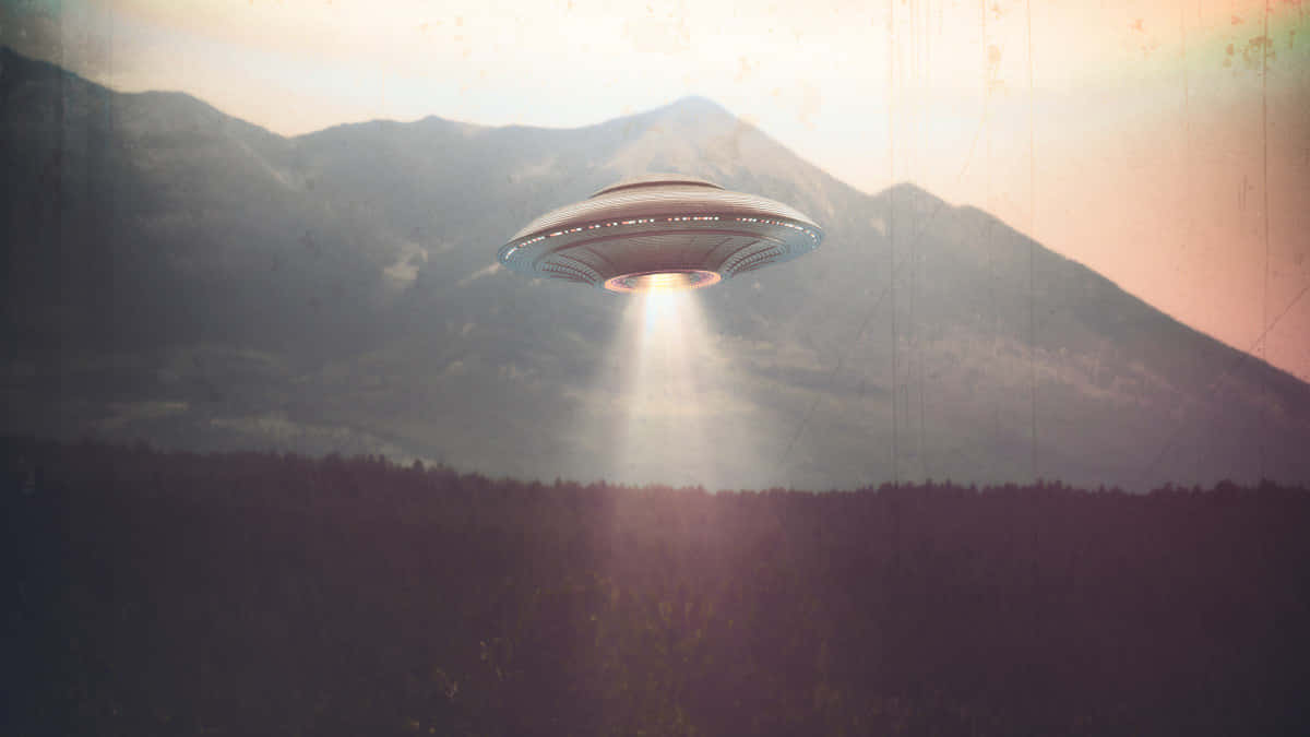  壁紙 — 一個發光的UFO懸浮在森林覆蓋的山谷上空，背景是山脈，溫暖的日落天空下。