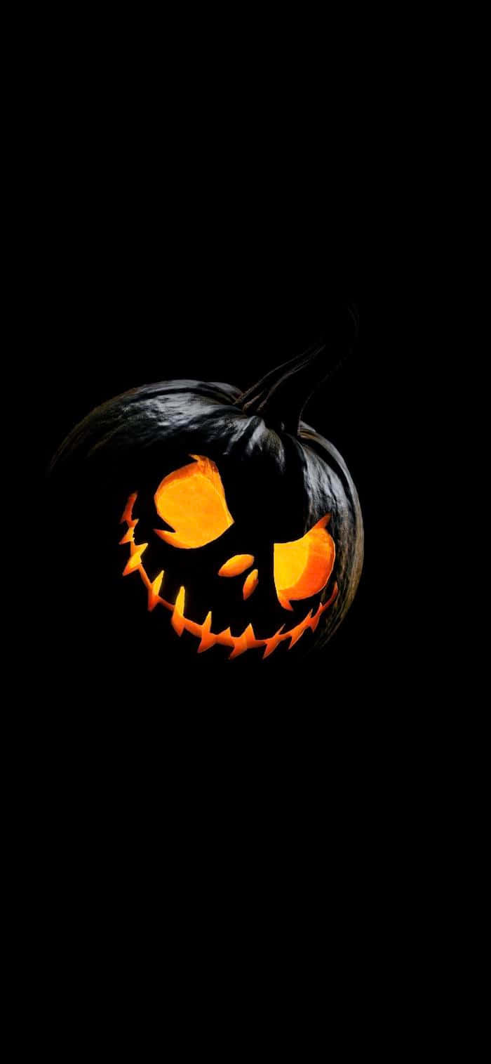 Minimalist Halloween 桌布 壁紙 — 一個發光的傑克南瓜燈，帶有鋸齒狀牙齒和發光的眼睛，漂浮在漆黑的背景上。