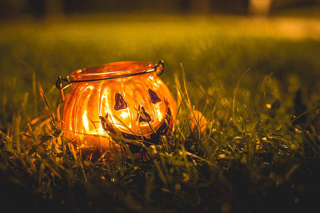 Cute Halloween Desktop 桌布 壁紙 — 一個發光的傑克南瓜燈，帶有雕刻的臉孔，夜晚放置在草地上，散發出溫暖的橙色光芒。