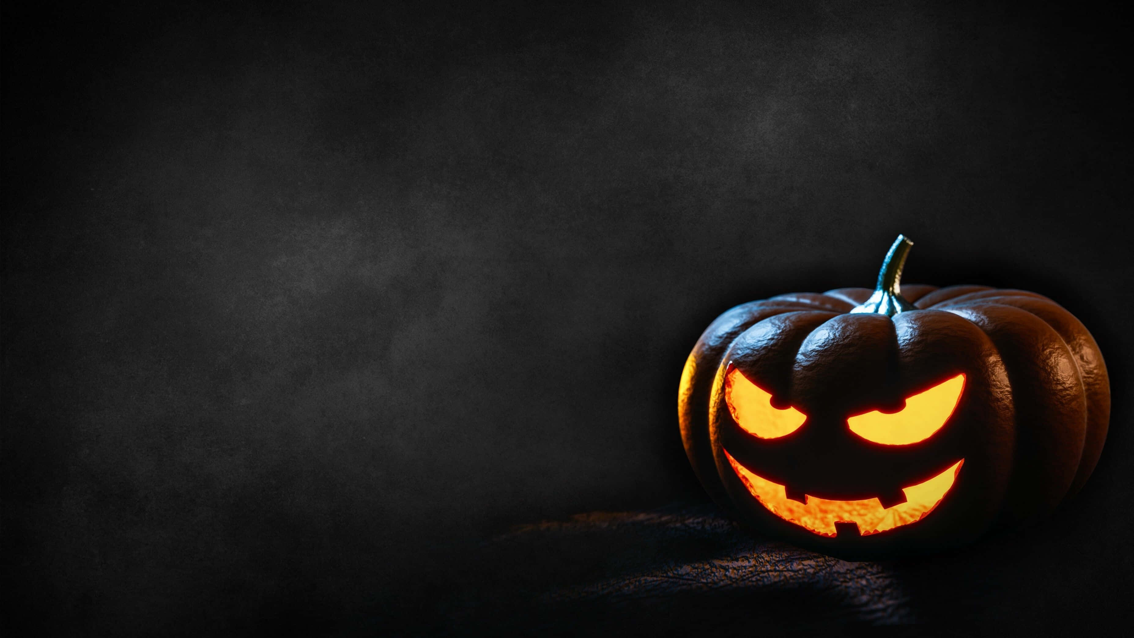 Minimalist Halloween 桌布 壁紙 — 一個發光的傑克南瓜燈，帶著兇惡的笑容，在煙霧繚繞的黑色背景上投射出詭異的橙色光芒。