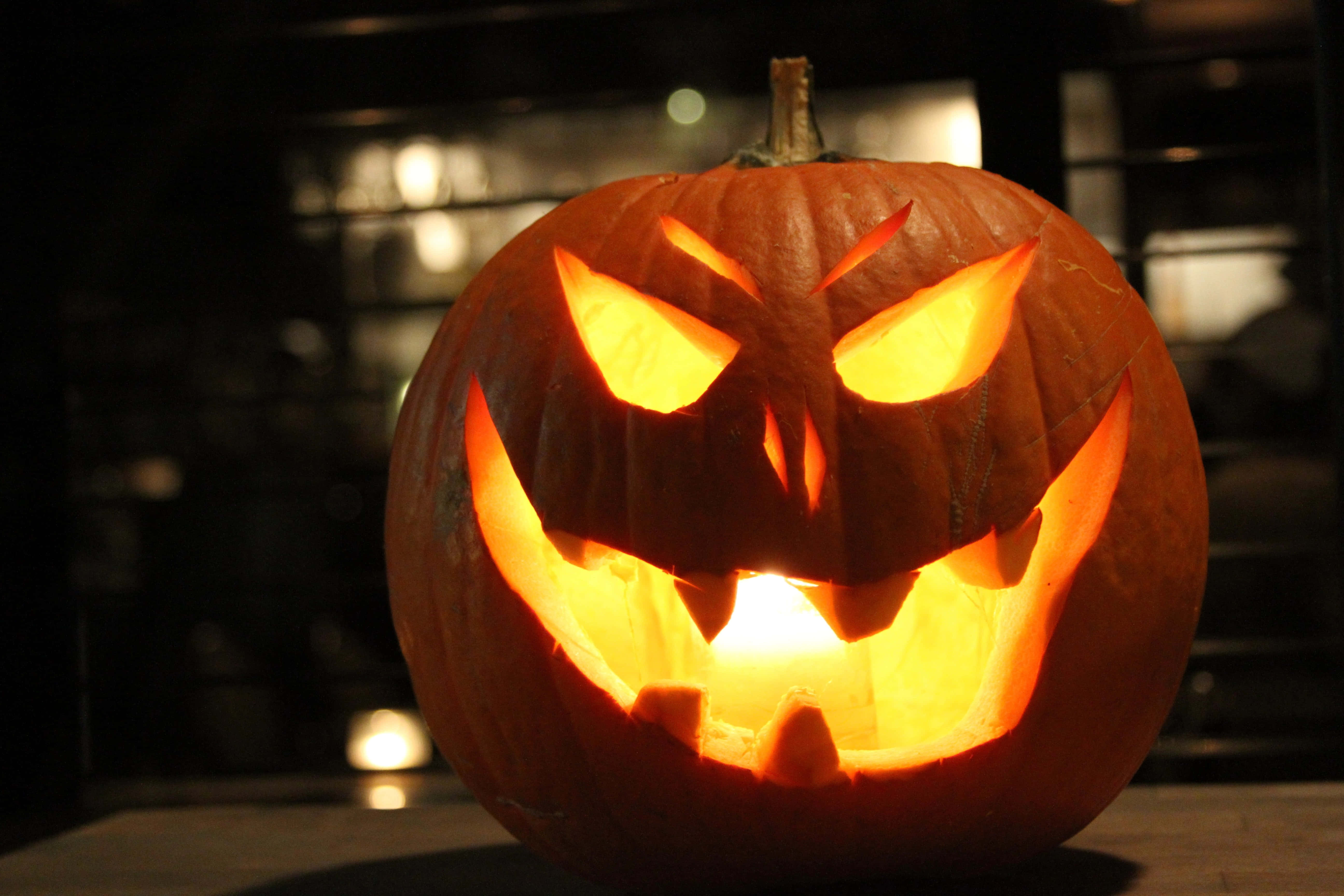 Jack O Lantern 桌布 壁紙 — 一個發光的傑克南瓜燈，帶著兇惡的笑容，用溫暖的橙色光芒照亮了黑暗的房間。