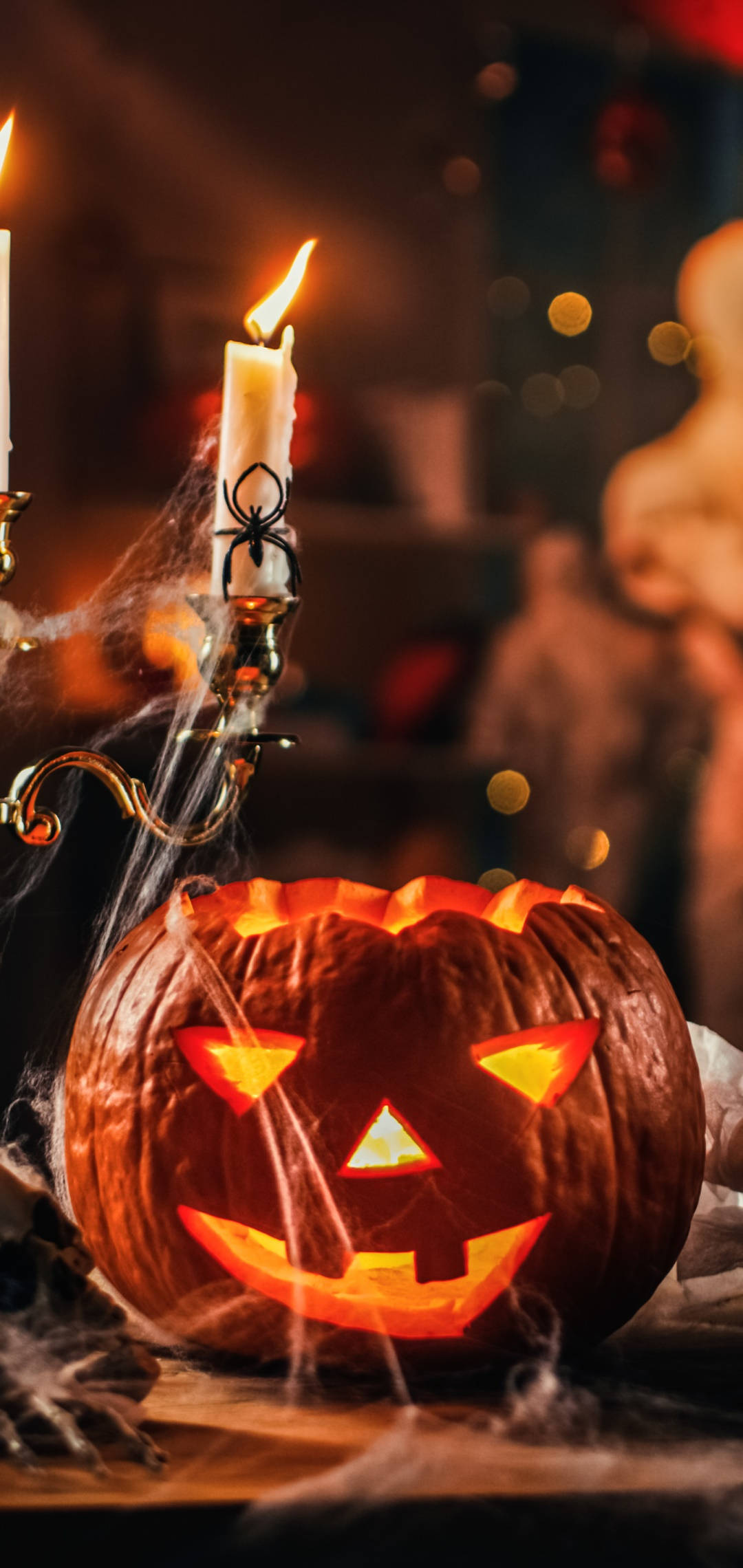 Halloween Phone 桌布 壁紙 — 一個發光的傑克南瓜燈，帶著邪惡的笑容，旁邊是一個佈滿蜘蛛網的燭台。