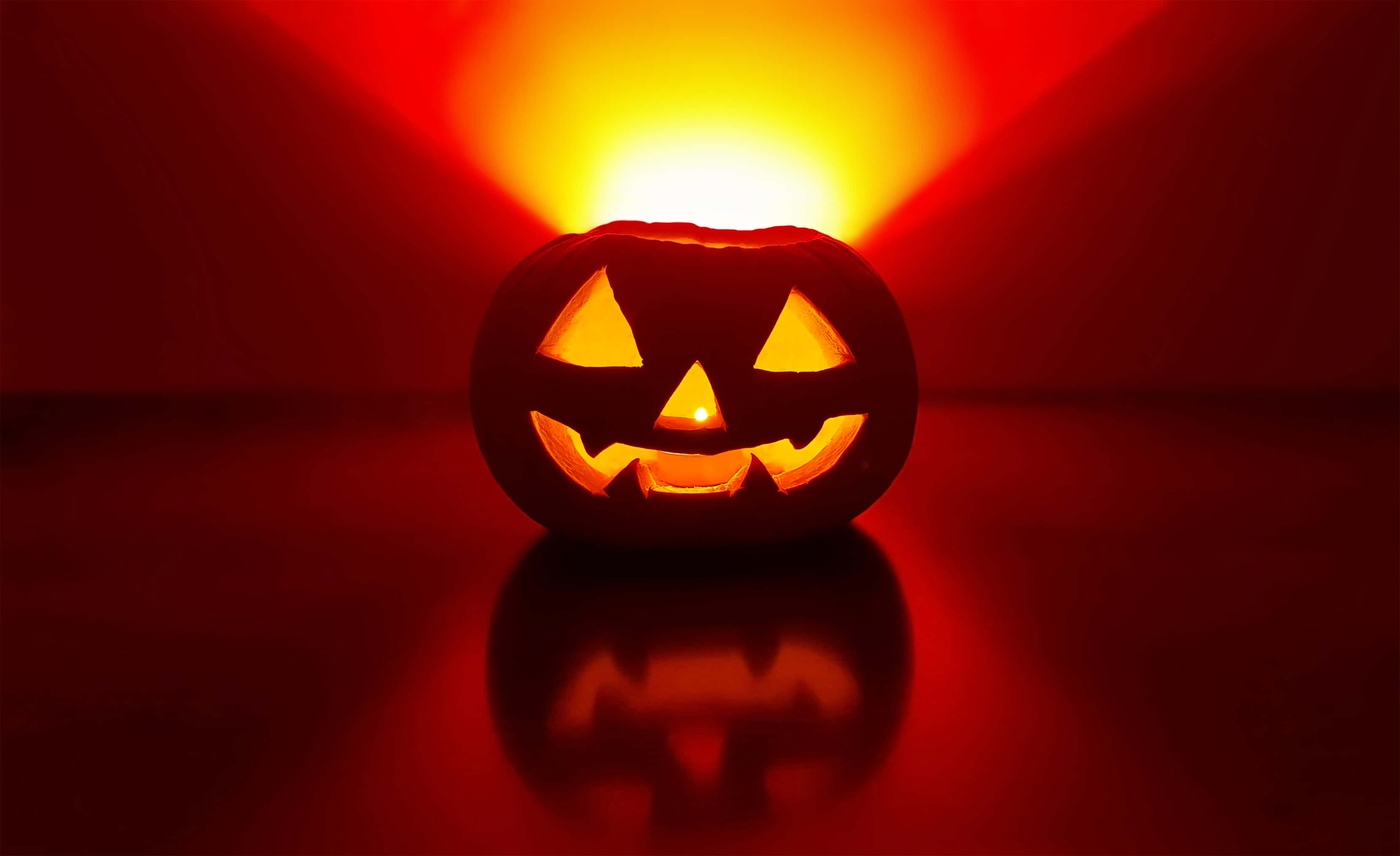 Halloween Crafts 桌布 壁紙 — 一個發光的傑克南瓜燈，裡面有蠟燭，在帶有反光表面的深紅色背景上投射出溫暖的橙色光芒。