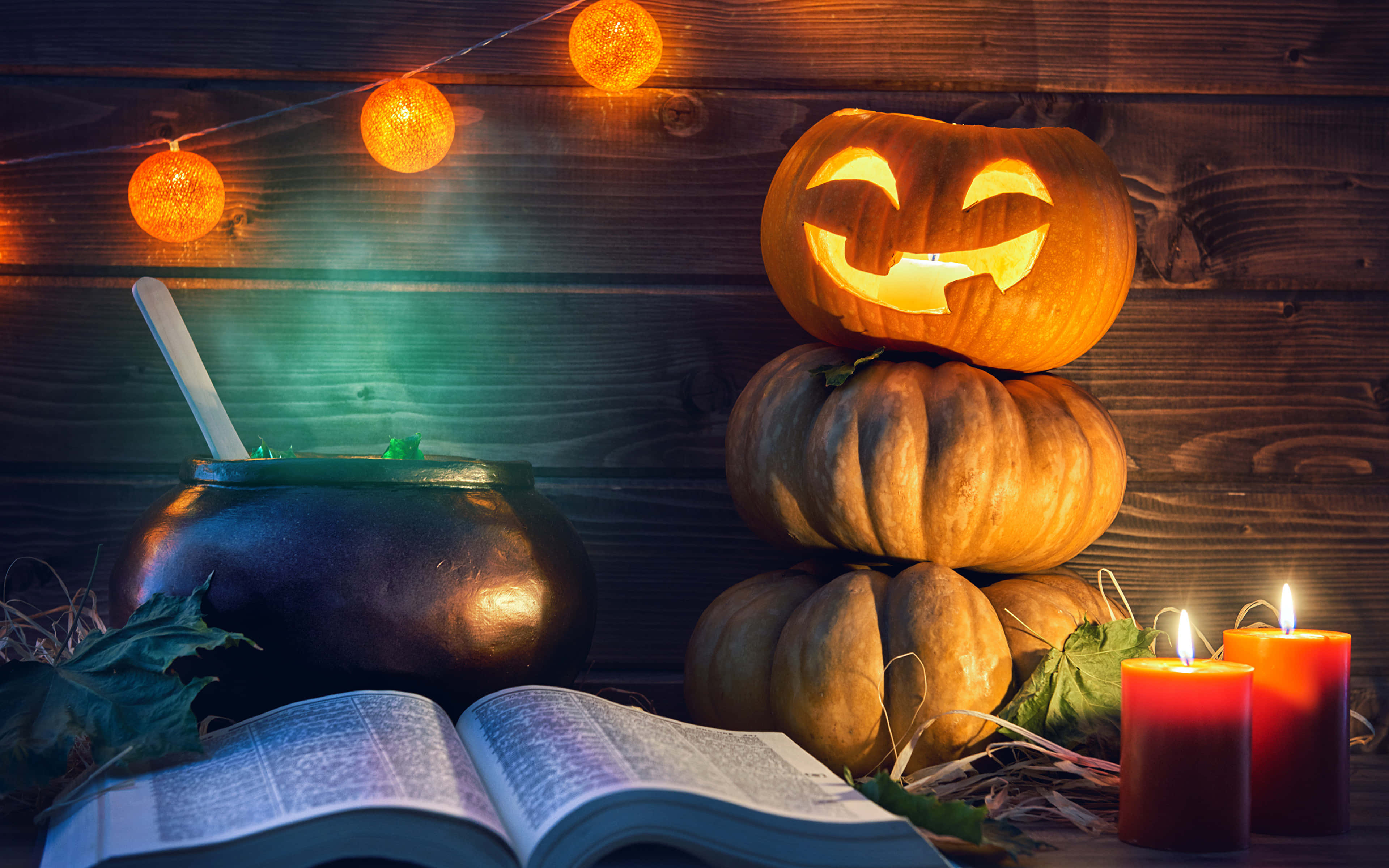 Halloween Books 桌布 壁紙 — 一個發光的傑克南瓜燈堆疊在南瓜上，旁邊有坩堝、蠟燭和一本打開的書，背景是質樸的木牆。
