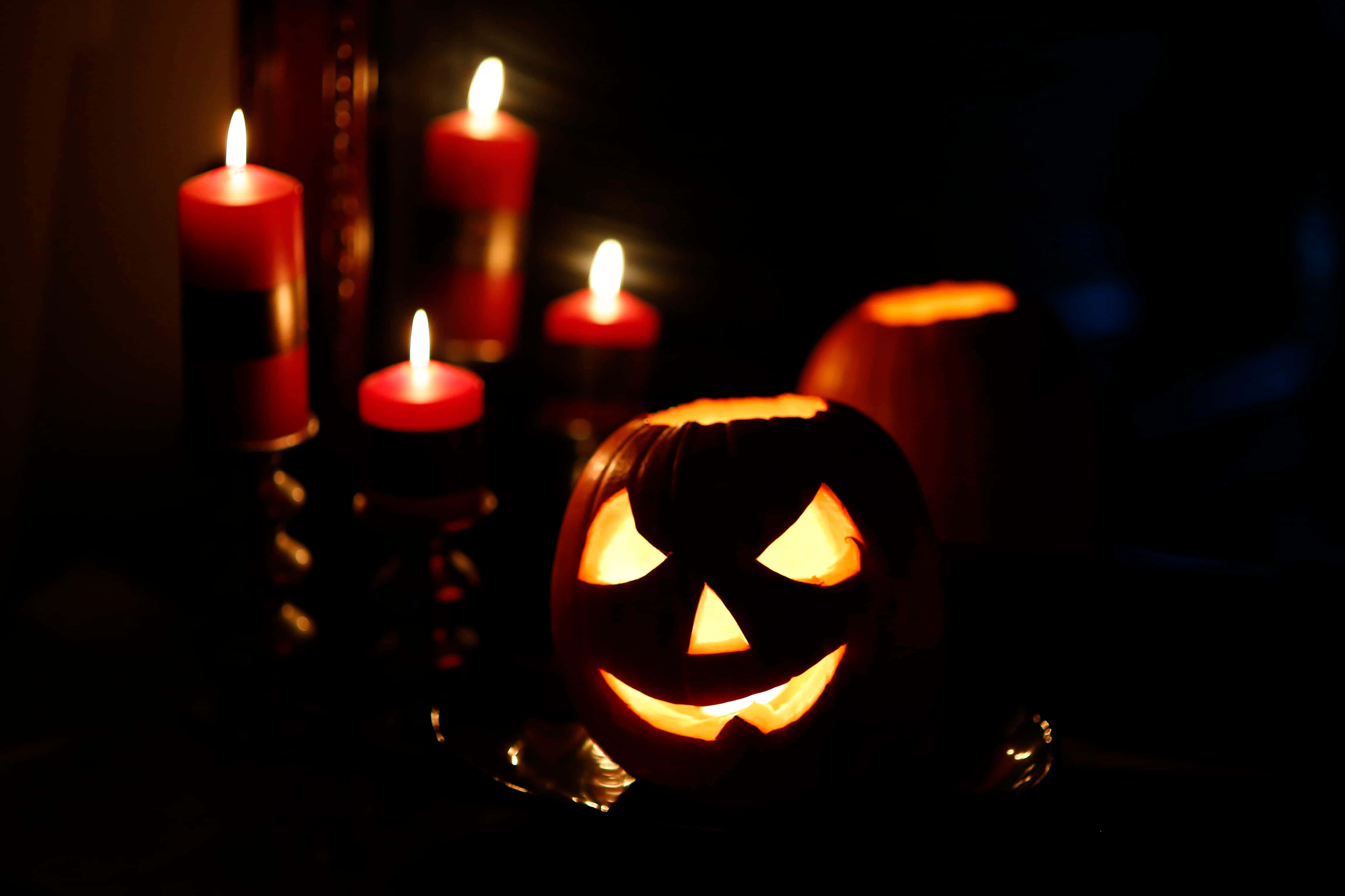 Halloween Candles 桌布 壁紙 — 一個發光的傑克南瓜燈帶著邪惡的笑容，坐在黑暗、充滿氣氛的萬聖節場景中，旁邊是閃爍的紅色蠟燭。