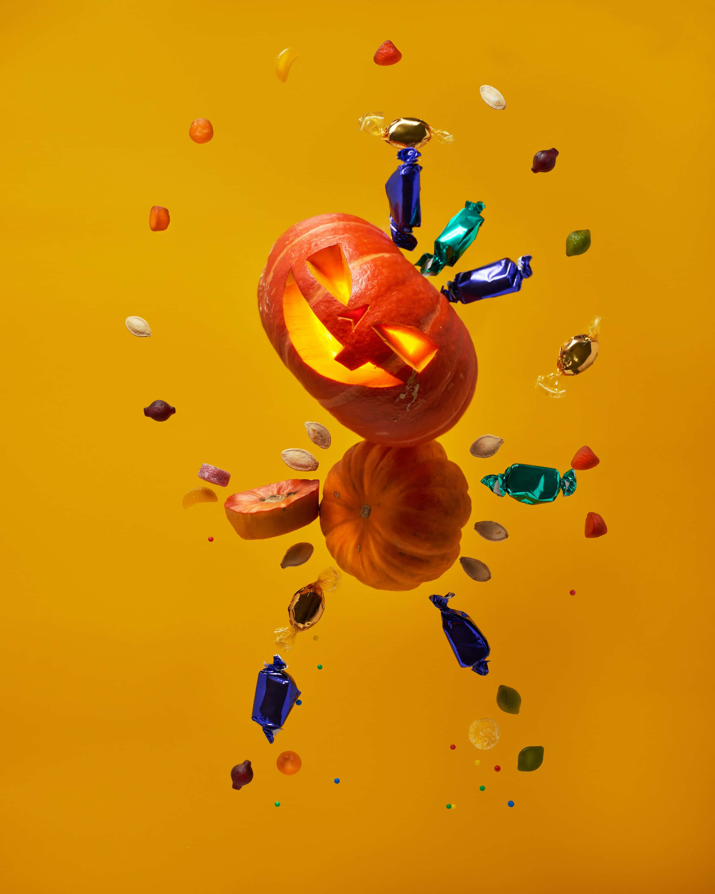 jack o'lantern 桌布 壁紙 — 一個發光的傑克南瓜燈漂浮在色彩繽紛的糖果和南瓜籽的爆發中，背景是溫暖的橙色。