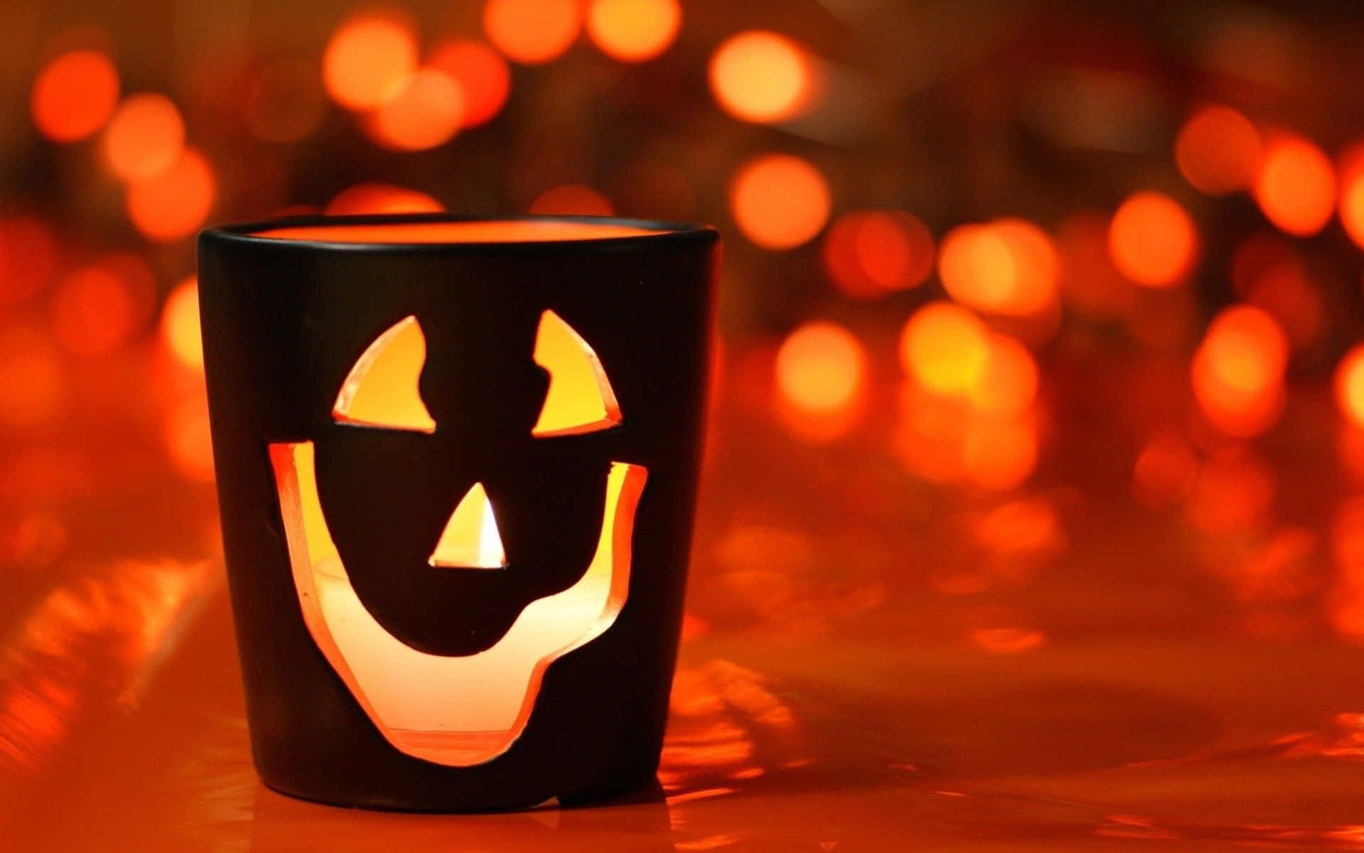 Funny Halloween 桌布 壁紙 — 一個發光的傑克南瓜燈燭台，帶有微笑的臉，在橙色燈光的散景背景下發出溫暖的光芒。