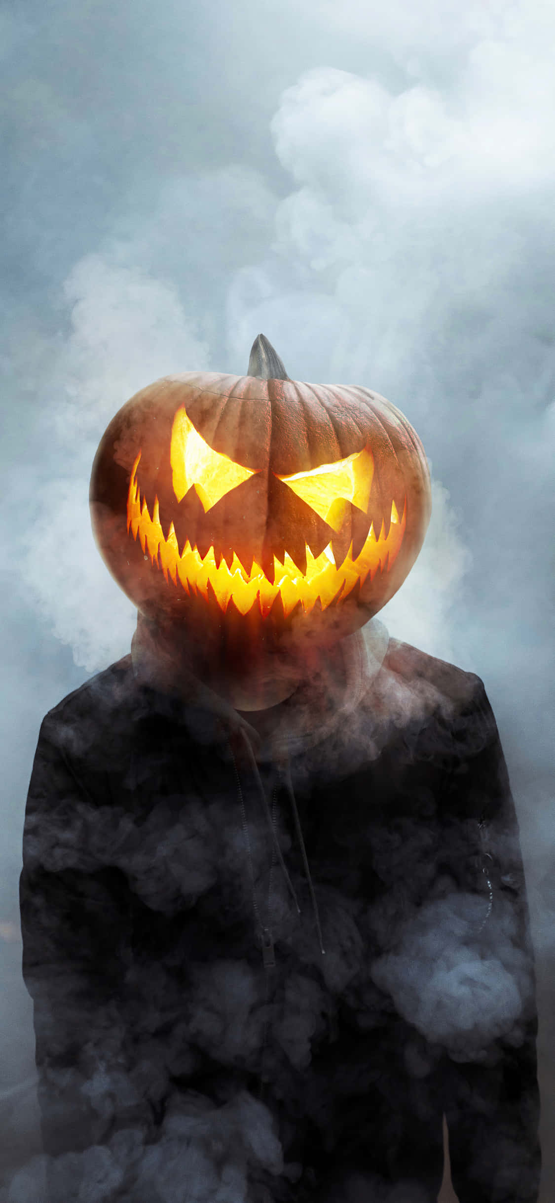 Jack O Lantern 桌布 壁紙 — 一個發光的傑克南瓜燈頭，帶有鋸齒狀牙齒和發光的眼睛，在霧濛濛的灰色煙霧中懸浮，背景多雲。