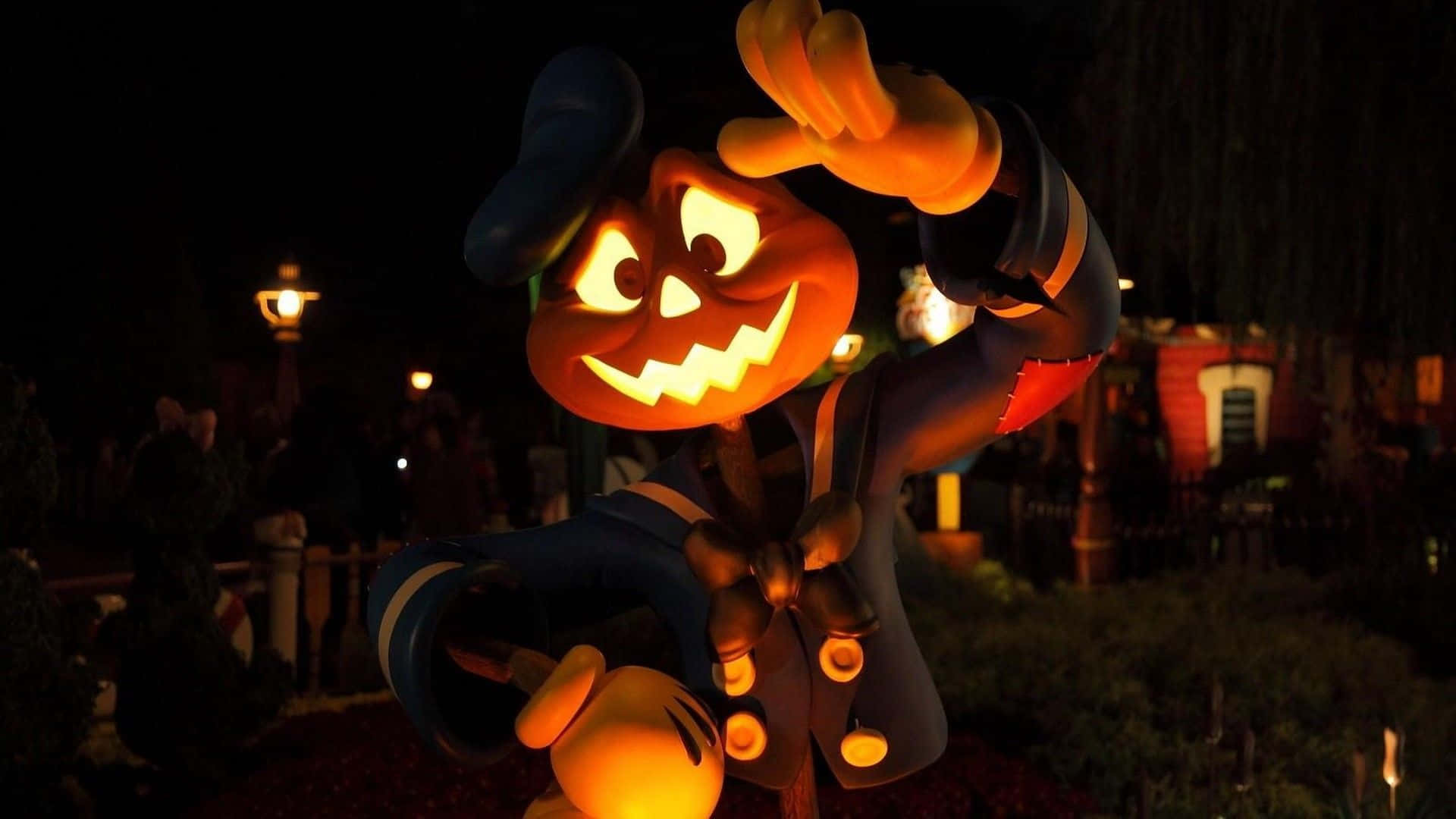 Halloween Costume 桌布 壁紙 — 一個發光的傑克南瓜燈頭米奇老鼠公仔在萬聖節主題公園環境中夜間愉快地揮手。