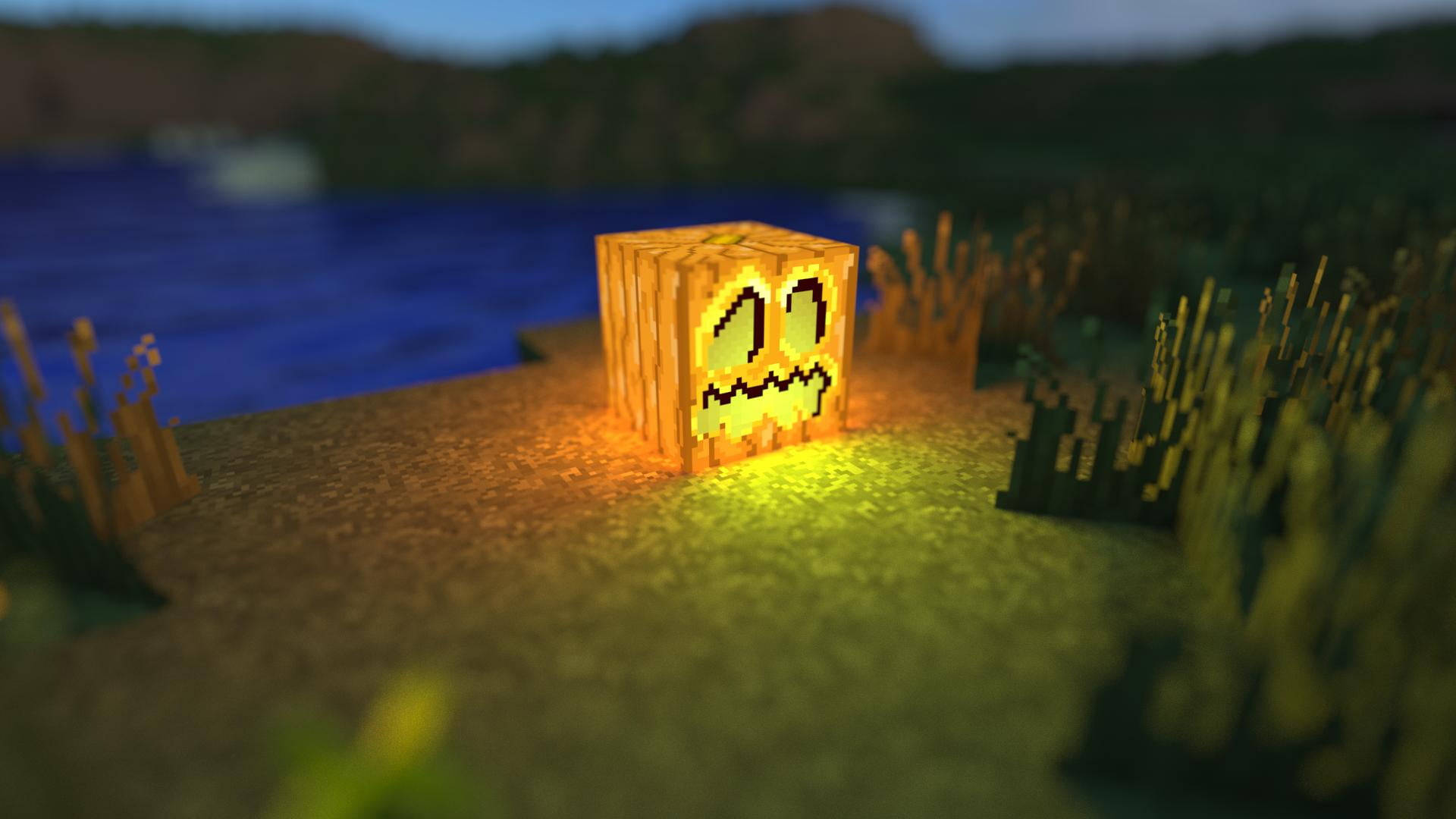 jack o'lantern 桌布 壁紙 — 一個發光的像素化南瓜燈立方體放在草地靠近水邊，背景是黃昏時分方塊狀的Minecraft風格景觀。