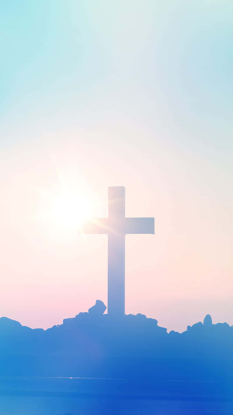 桌布 壁紙 — 一個發光的十字架在平靜的水面和岩石地形上，以柔和的日出天空為背景形成剪影。