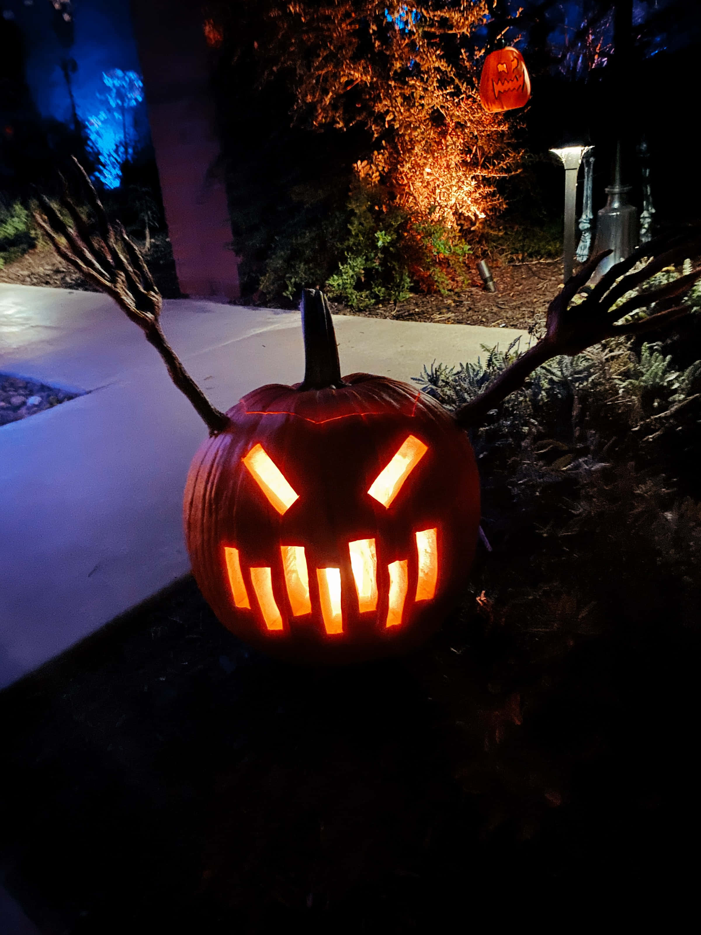 jack o'lantern 桌布 壁紙 — 一個發光的南瓜，帶有兇惡的眼睛和牙齒，夜晚坐在人行道上，手臂像爪子一樣伸出。