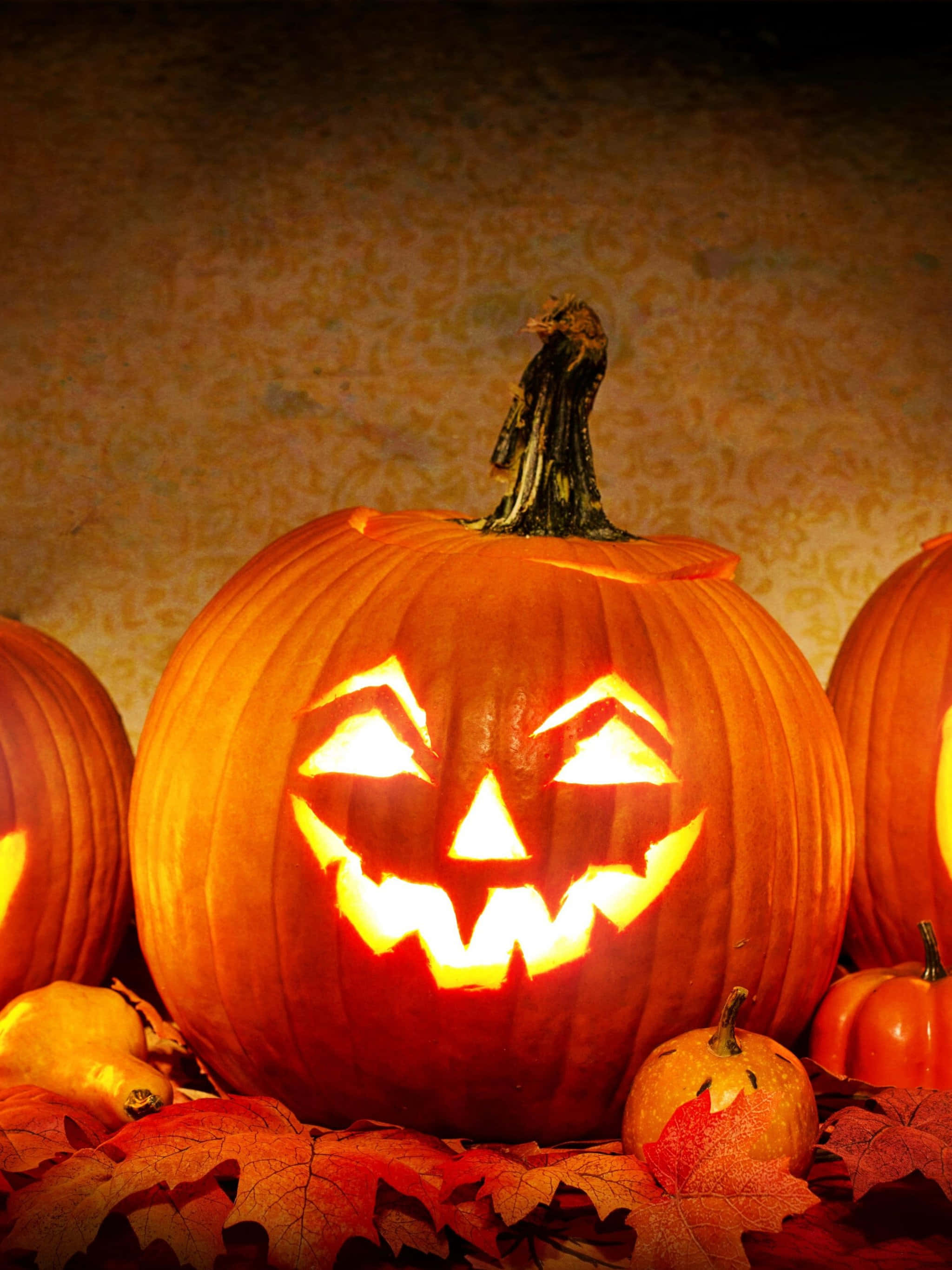 Pumpkin 桌布 壁紙 — 一個發光的南瓜燈露出邪惡的笑容，坐在秋天的樹葉和南瓜之間，背景是帶紋理的牆壁。
