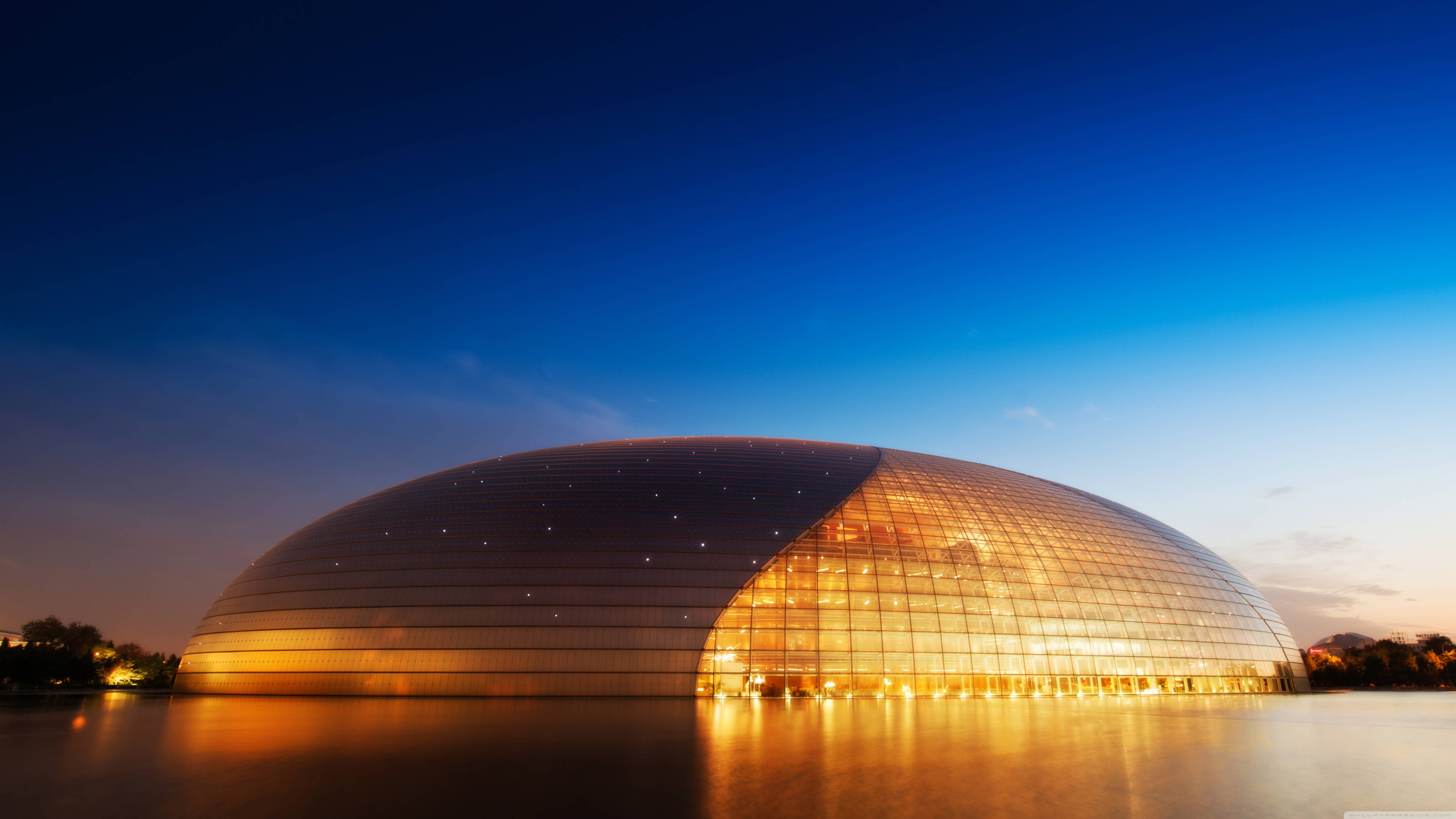 Beijing 桌布 壁紙 — 一個發光的圓頂音樂廳在深藍色暮色天空下溫暖地倒映在水面上。