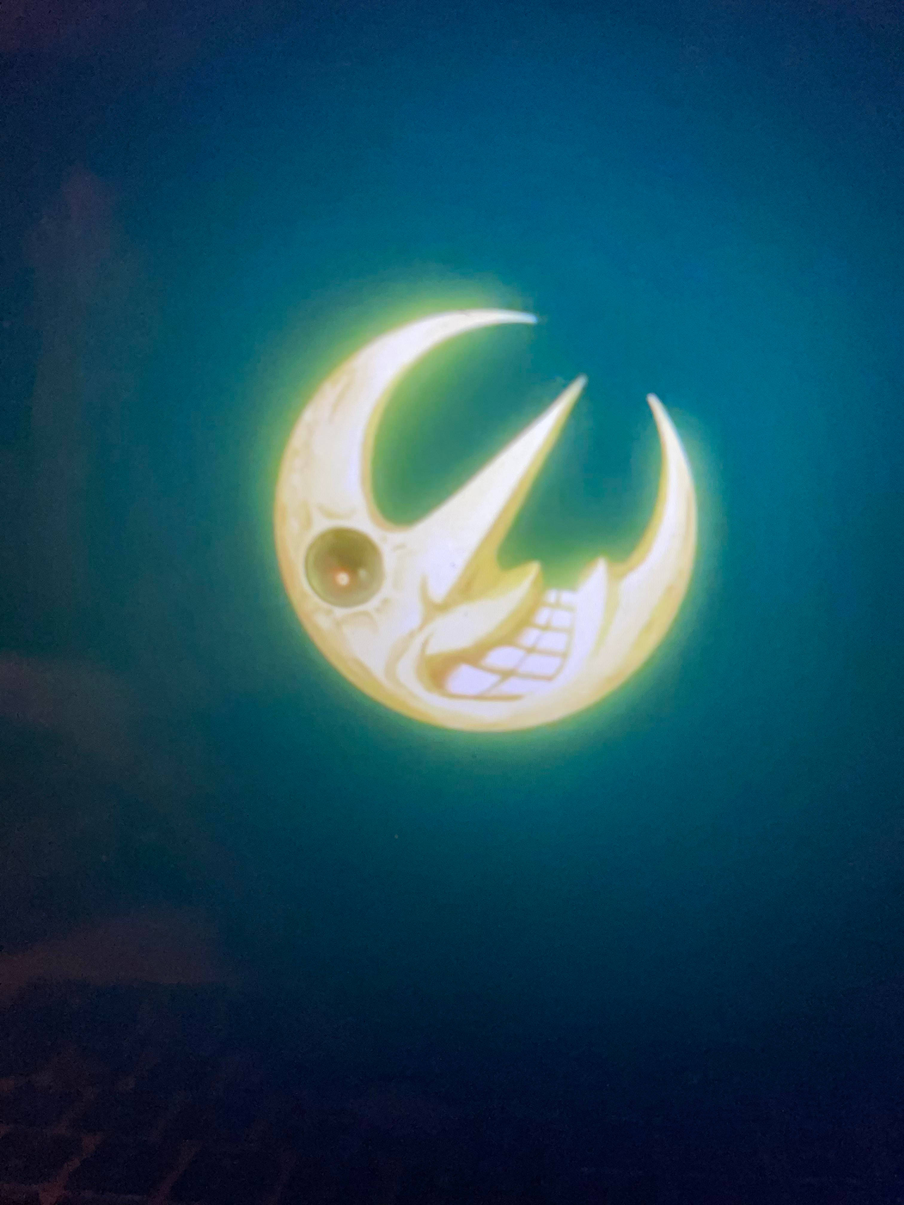 soul eater moon 桌布 壁紙 — 一個發光的彎月，帶有卡通臉和尖銳的牙齒，在深青色背景上明亮地閃耀。