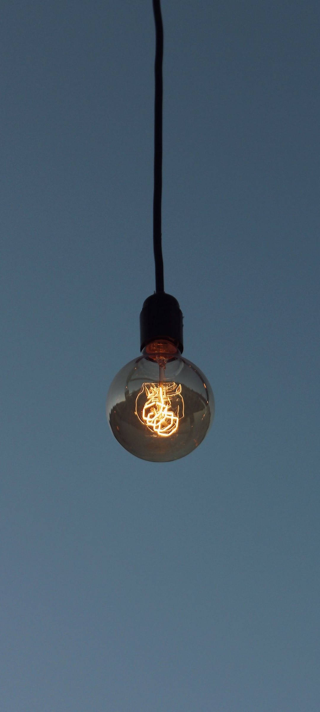 Light 桌布 壁紙 — 一個發光的復古燈泡懸掛在深邃的暮色天空中，在寧靜的夜晚散發出溫暖的光芒。