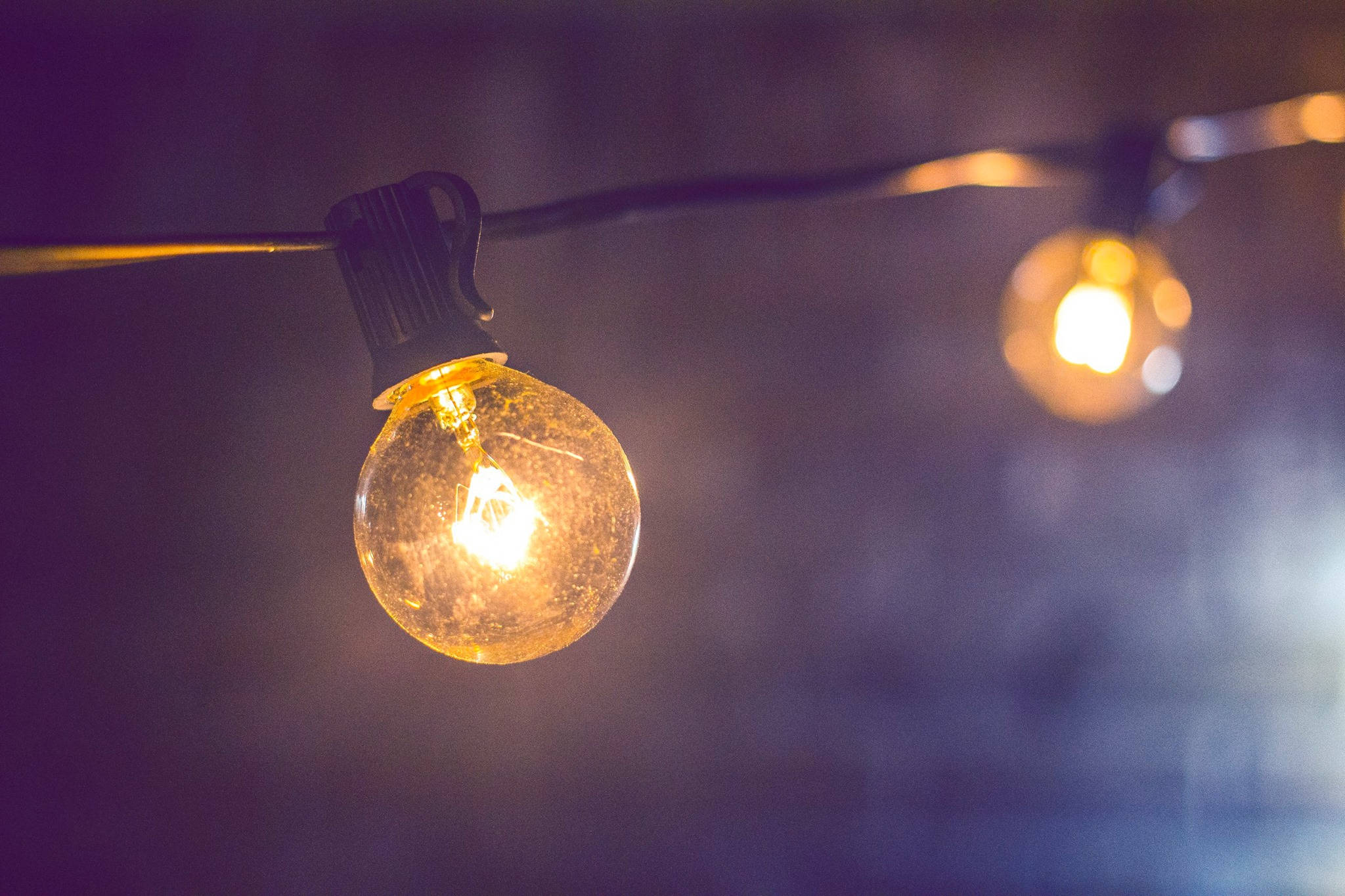 Light Bulb 桌布 壁紙 — 一個發光的復古燈泡掛在繩子上，背景是深紫色模糊的。
