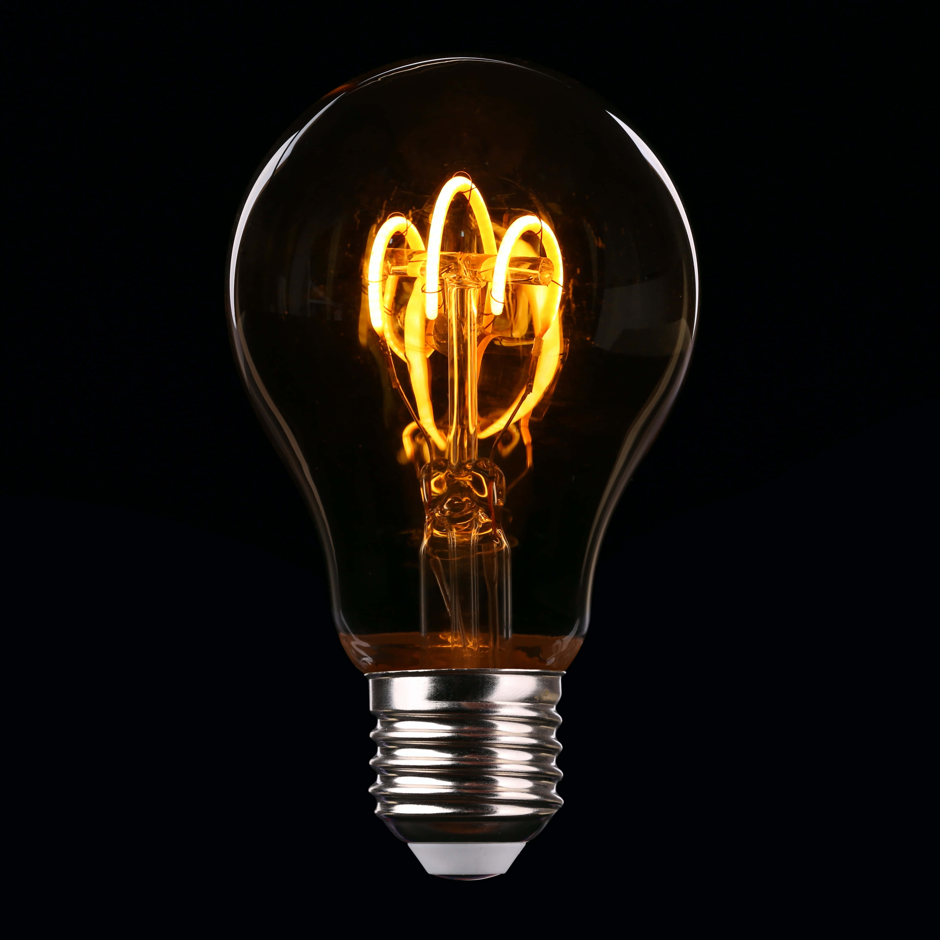 Light 桌布 壁紙 — 一個發光的復古燈絲燈泡，在純黑色背景上發出溫暖的琥珀色光芒。