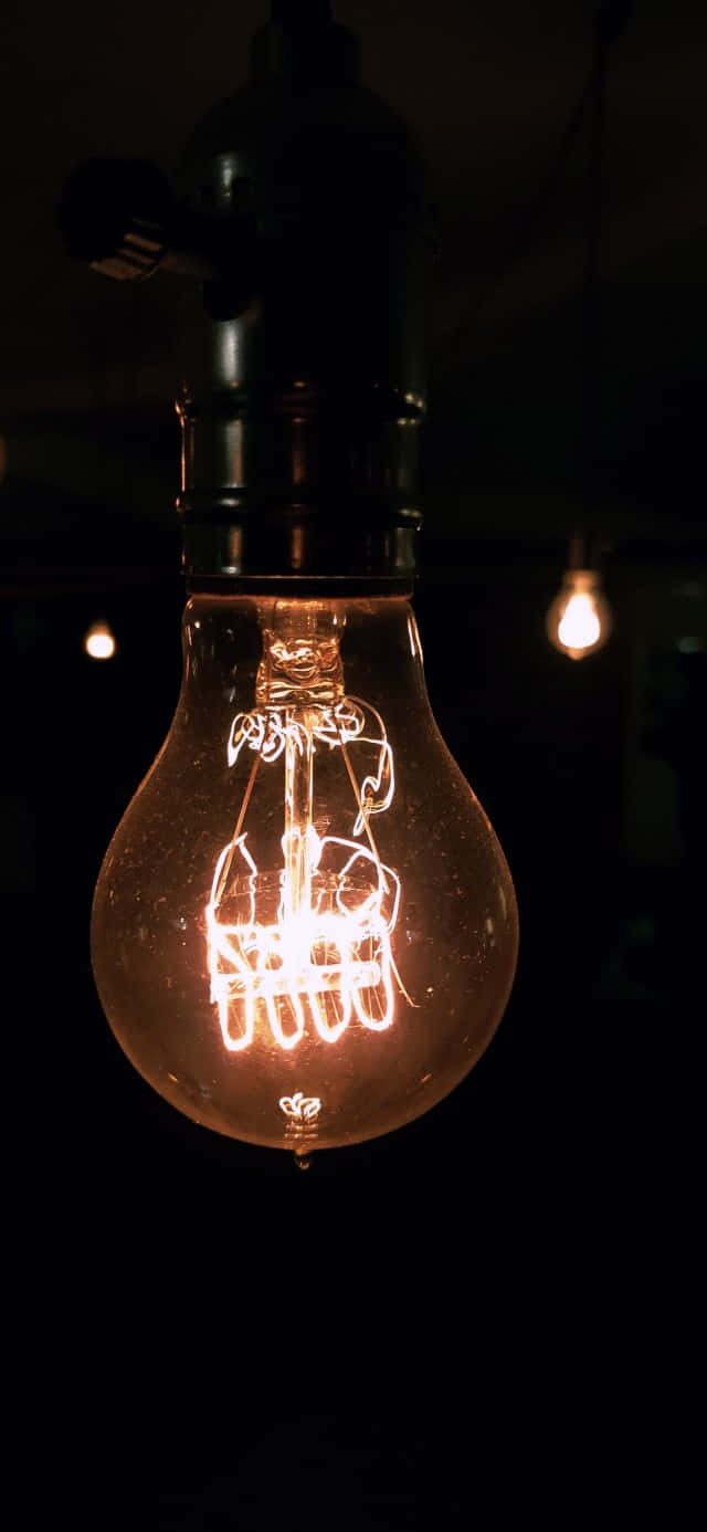 電力 桌布 壁紙 — 一個發光的復古燈絲燈泡懸掛在黑暗中，溫暖的光線投射出柔和的陰影，並凸顯內部複雜的線圈。