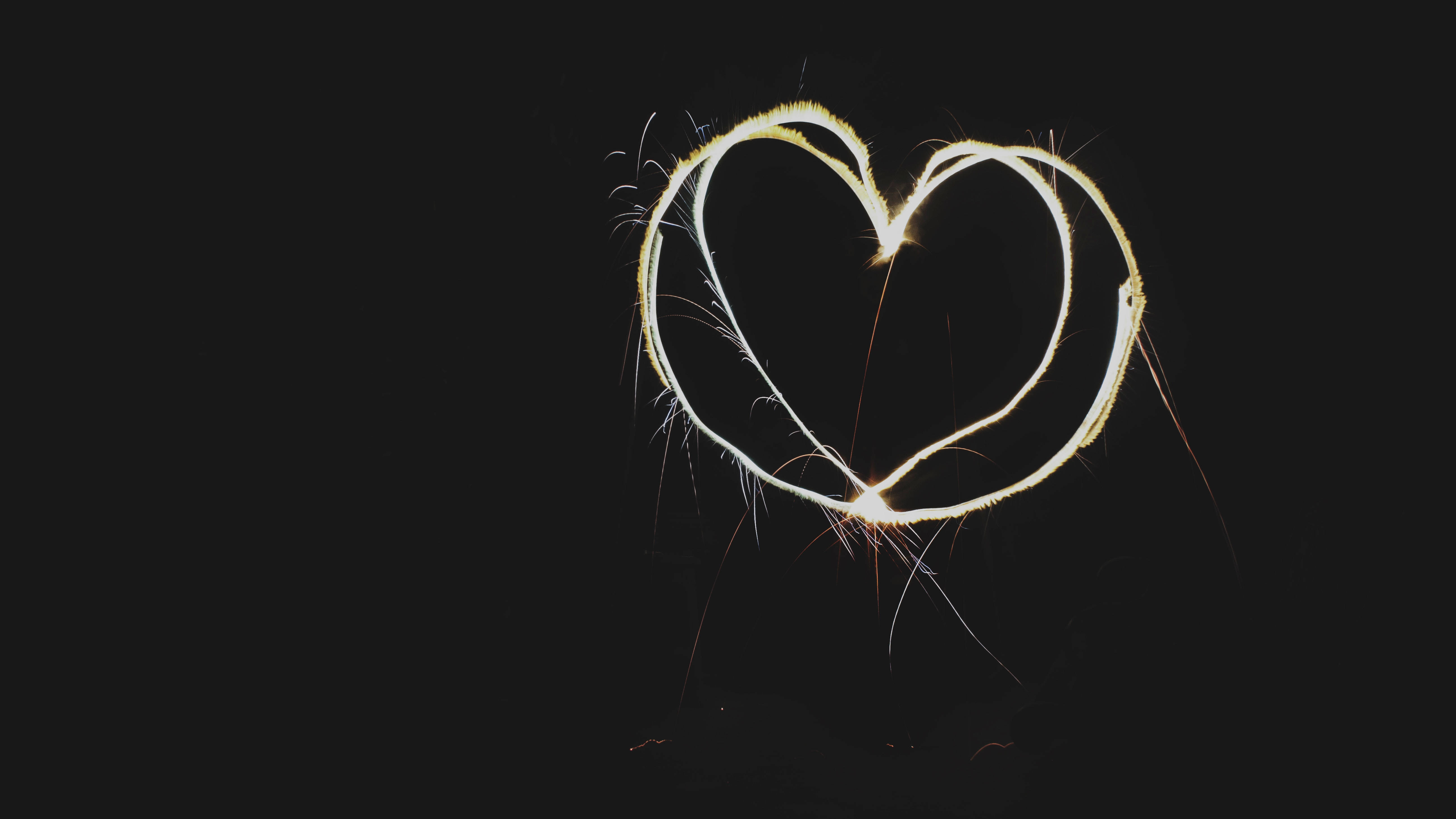 Dark Heart 桌布 壁紙 — 一個發光的愛心形狀煙火棒在純黑色背景上留下明亮的火花。