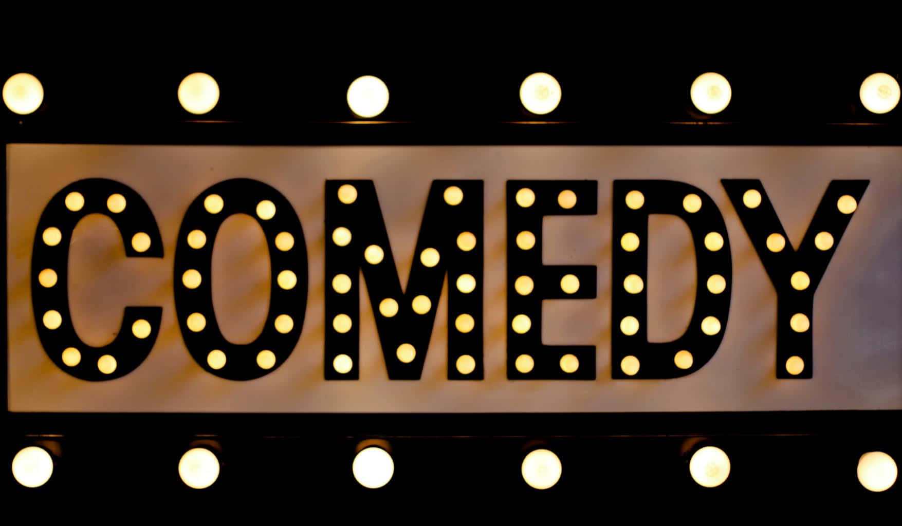comedy 桌布 壁紙 — 一個發光的招牌，以粗體字母拼出COMEDY，周圍環繞著溫暖的圓形燈泡，背景為深色。