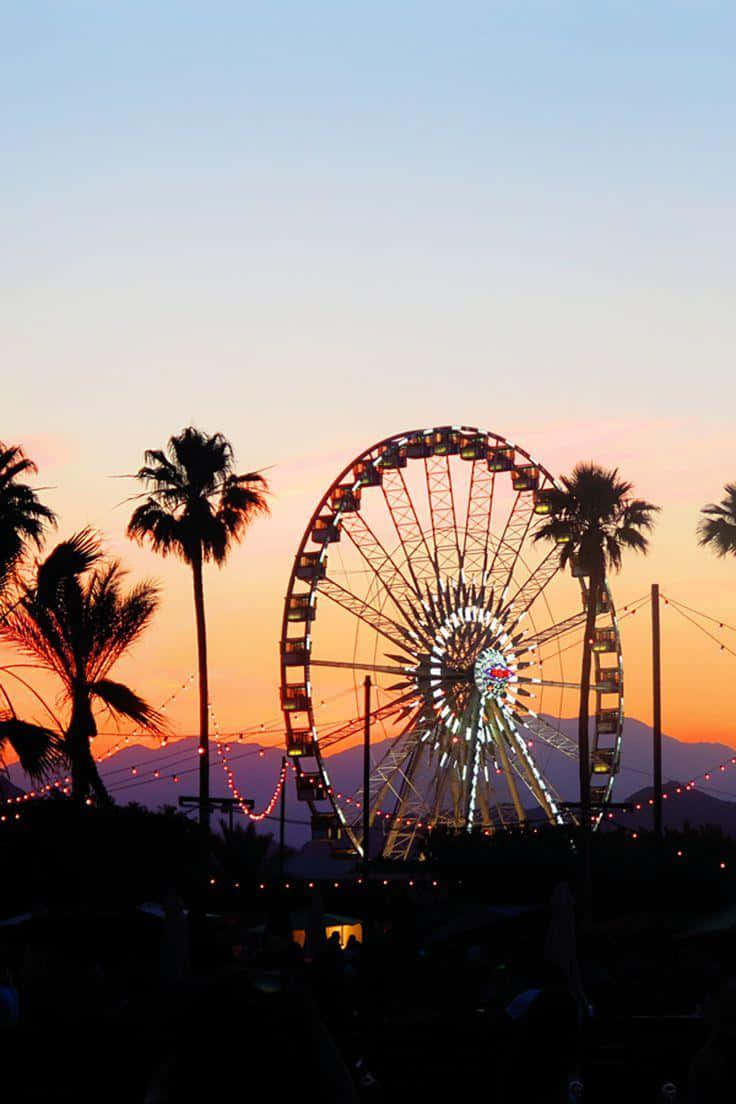 Coachella 桌布 壁紙 — 一個發光的摩天輪在棕櫚樹和遠山環繞的鮮豔日落天空下形成剪影。