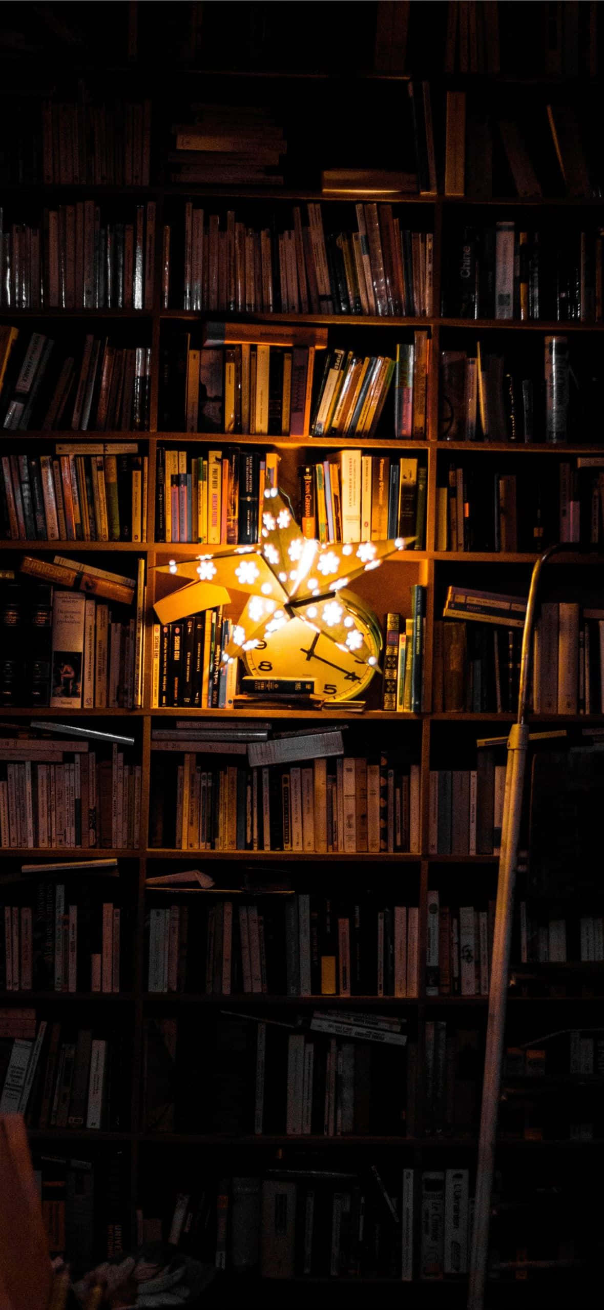 books 桌布 壁紙 — 一個發光的星形燈，帶有鐘面，照亮了裝滿書本的黑暗書架。