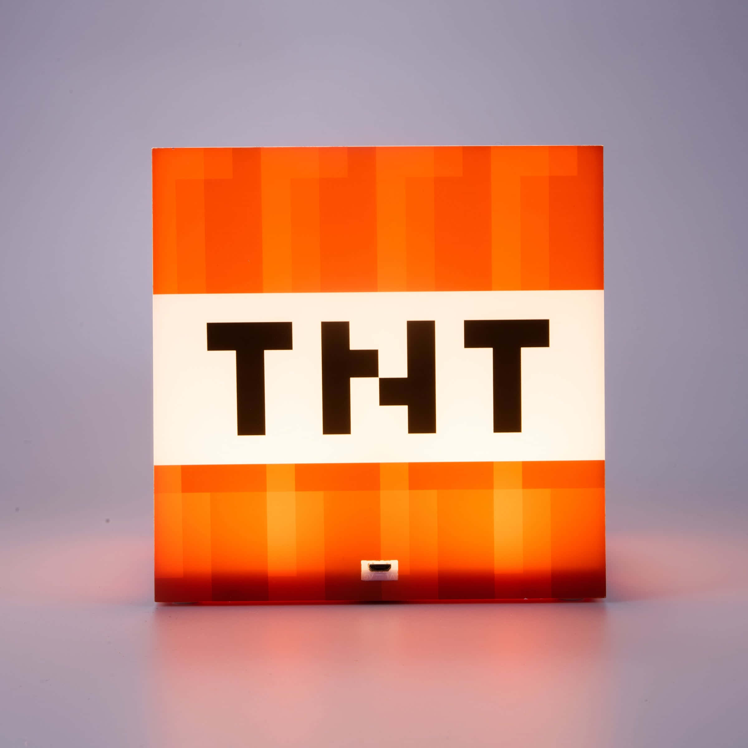 我的世界 TNT 桌布 壁紙 — 一個發光的橙色像素化TNT方塊燈，帶有粗體黑色字母，在灰色表面上投射溫暖的光線。