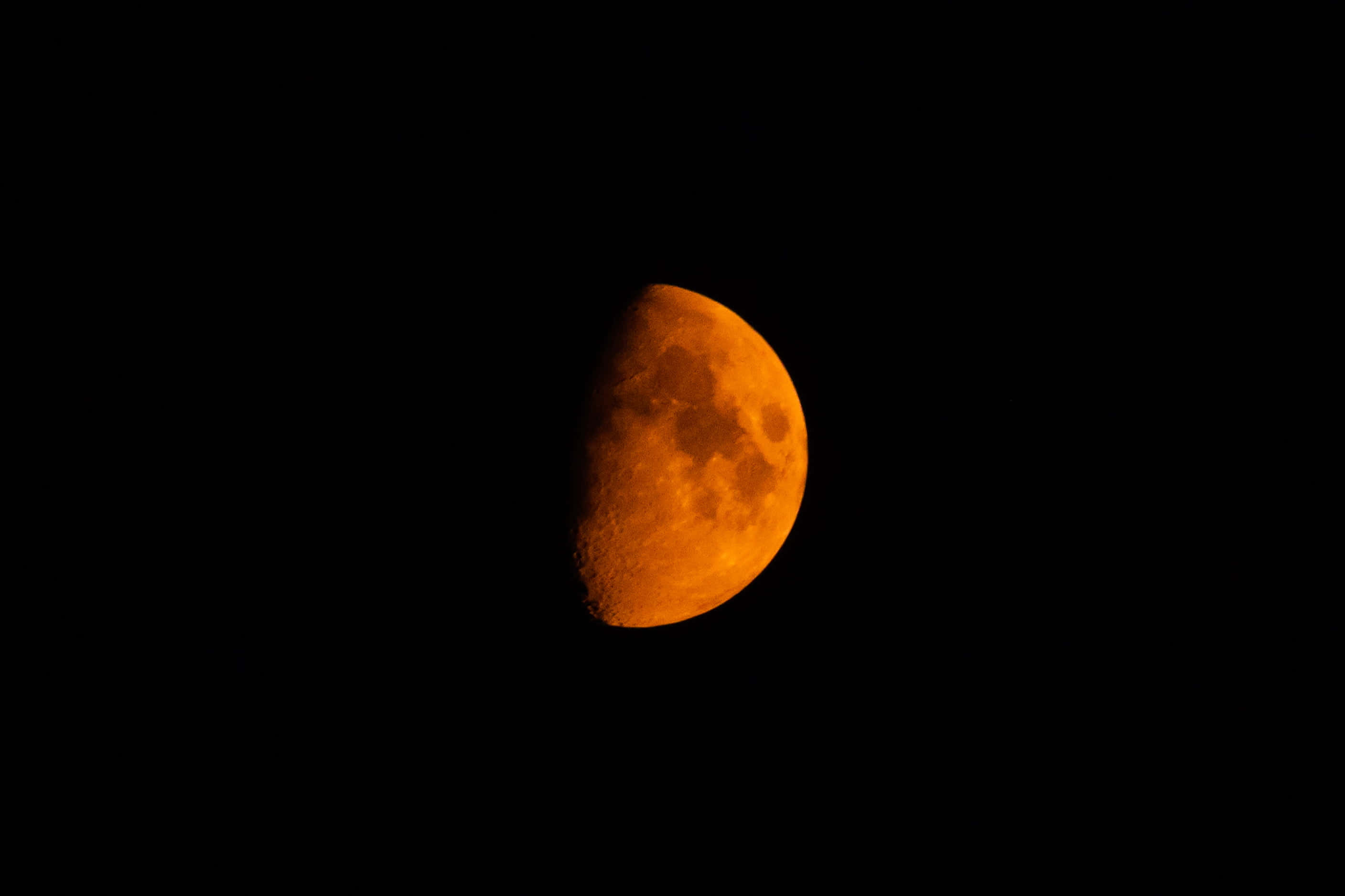 Half Moon 桌布 壁紙 — 一個發光的橙色半月獨自懸掛在漆黑的夜空，可見隕石坑和紋理。