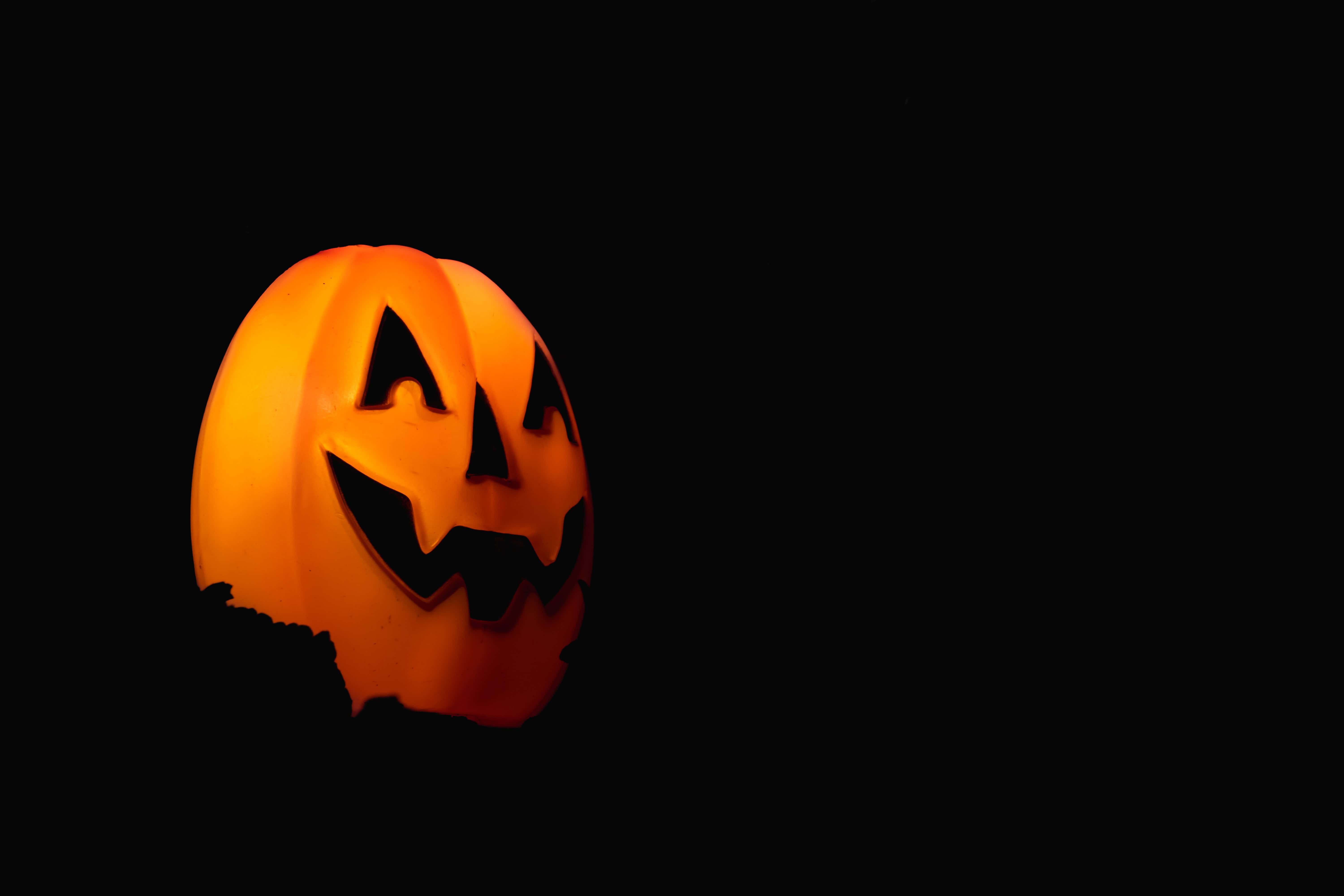 jack o'lantern 桌布 壁紙 — 一個發光的橙色南瓜燈，雕刻著兇惡的笑容，在漆黑的背景下閃耀。