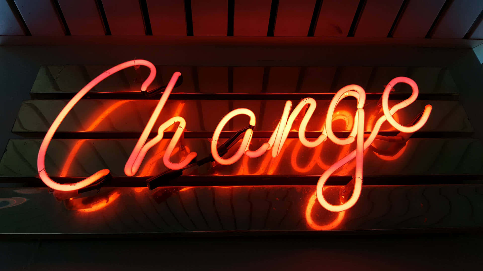 美學 桌布 壁紙 — 一個發光的橙色霓虹燈牌，上面拼寫著 'Change'，將溫暖的光線投射到其後方的深色木條上。