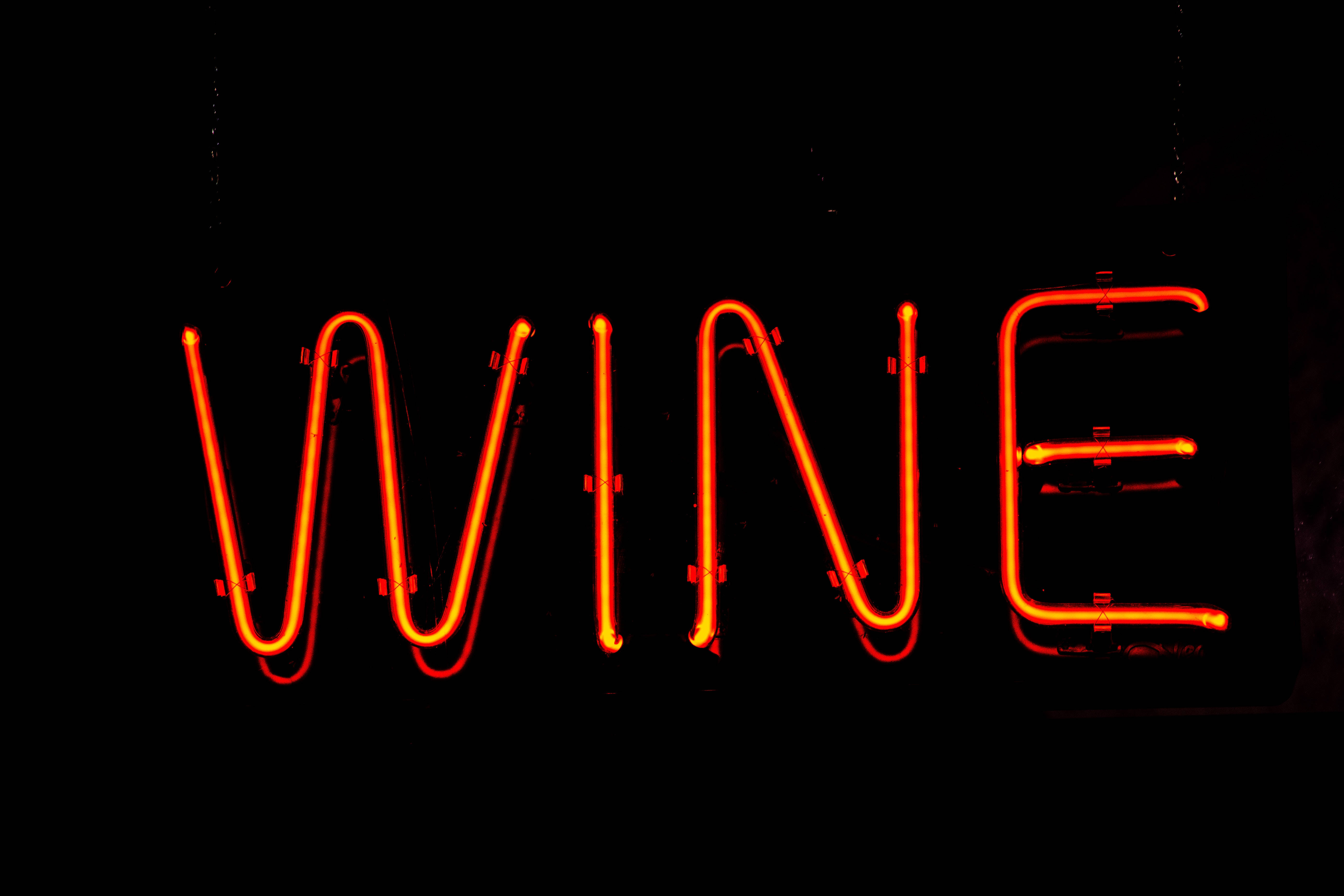 neon sign 桌布 壁紙 — 一個發光的橙色霓虹燈牌，在漆黑背景上拼出 WINE。