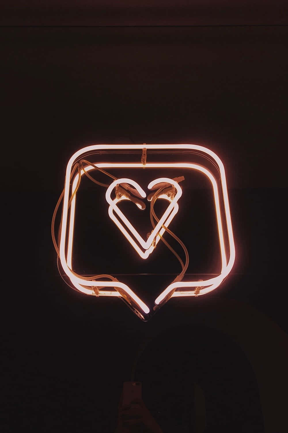 Neon Light 桌布 壁紙 — 一個發光的橙色霓虹燈牌，形狀像對話框，裡面有一顆心，掛在深色牆上。