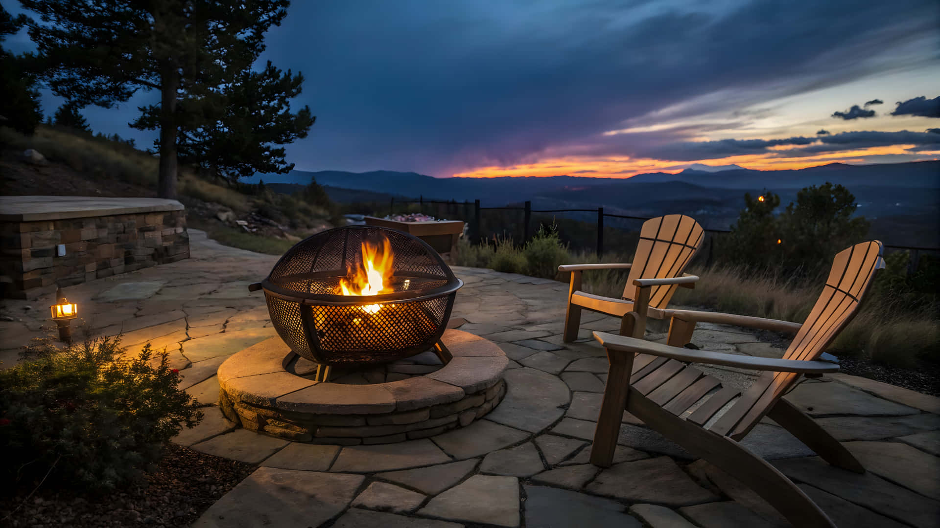 Outdoor fire pit with chairs at dusk overlooking mountains and sunset 壁紙 — 一個發光的火坑在石頭露臺上，有兩張木椅，面向山日落，天空戲劇性的暮色。