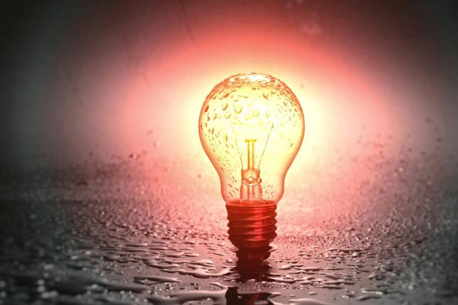 簡約手機 桌布 壁紙 — 一個發光的燈泡帶有水珠，放在潮濕的表面上，在黑暗背景下投射出溫暖的紅色光芒。
