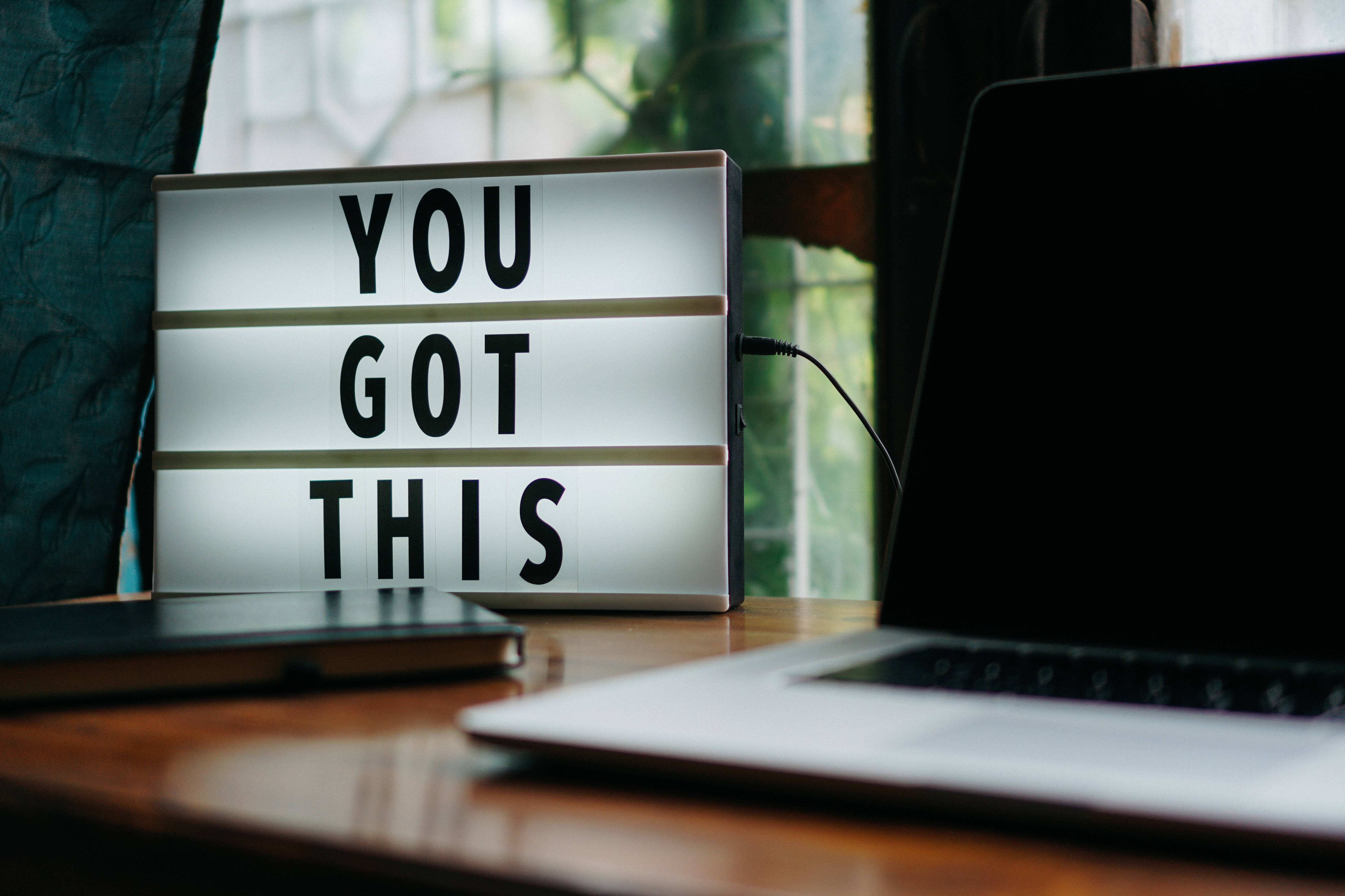激勵 桌布 壁紙 — 一個發光的燈箱顯示「YOU GOT THIS」，放在木桌上，旁邊有筆記型電腦和筆記本，靠近窗戶。