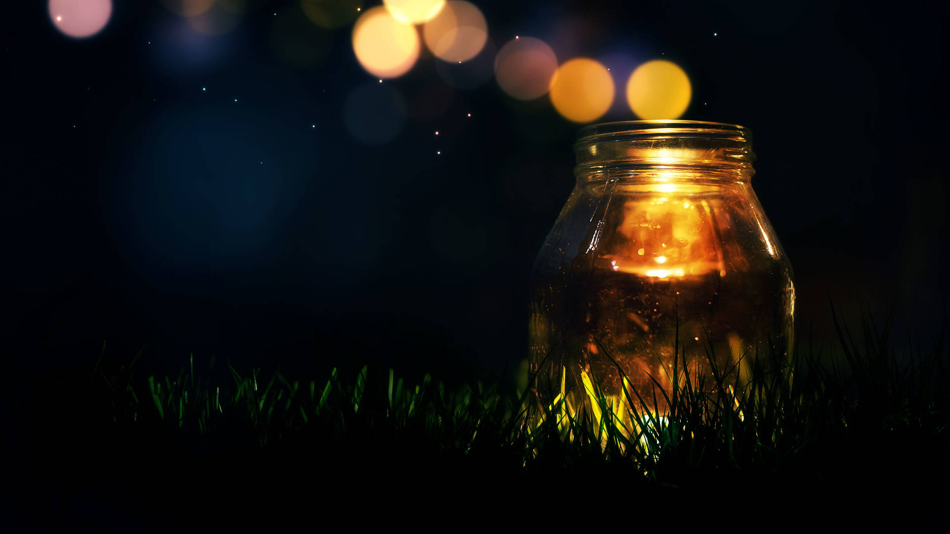 Light 桌布 壁紙 — 一個發光的玻璃瓶燈籠放在草地上，星空下遠處有溫暖的散景燈光。