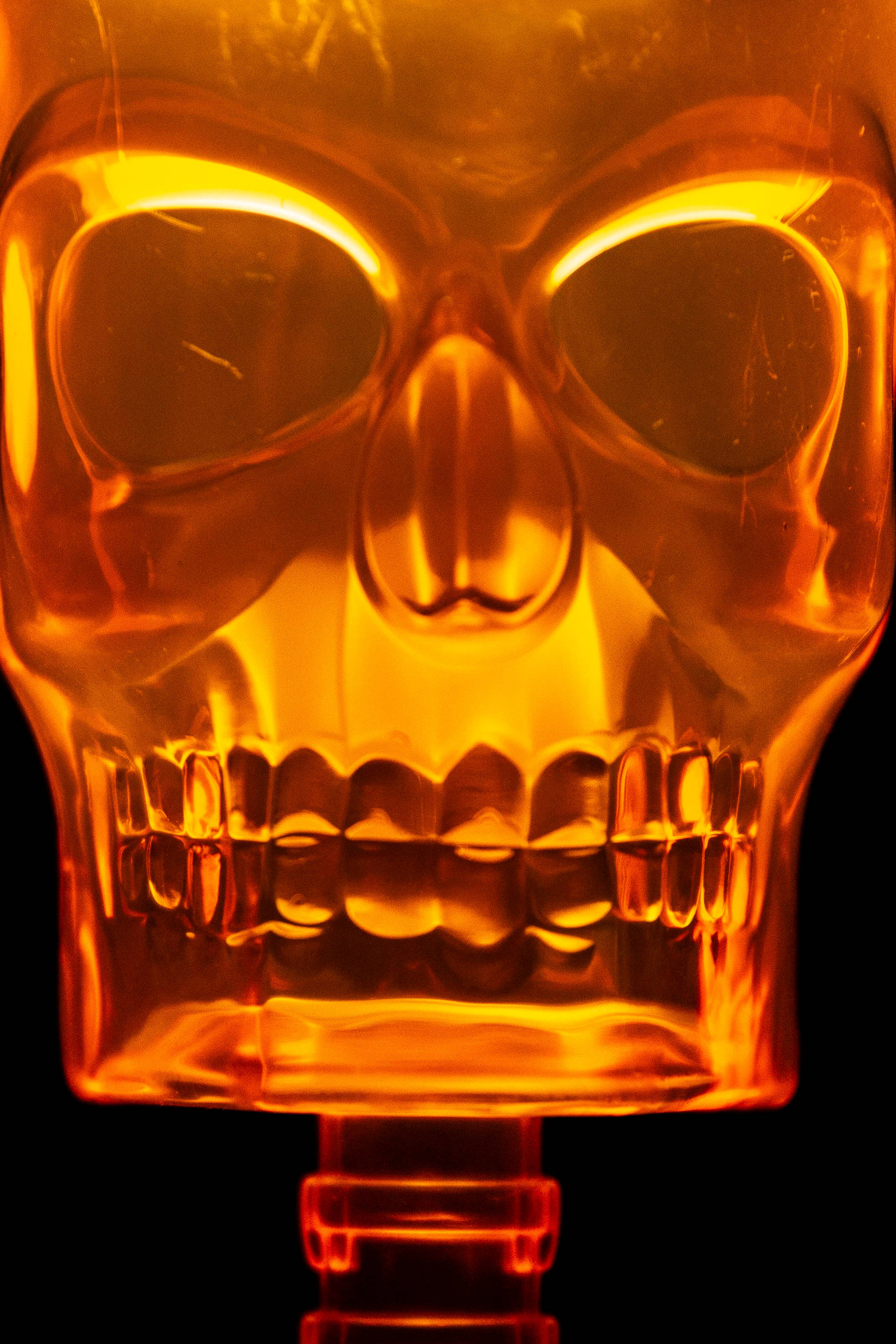 skulls 桌布 壁紙 — 一個發光的琥珀色骷髏形狀瓶子，從內部照亮，背景為黑色。