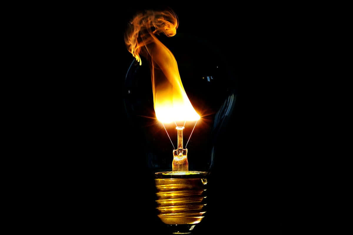 Light 桌布 壁紙 — 一個發光的白熾燈泡，其燈絲上冒出熾熱的橙色火焰，背景漆黑一片。