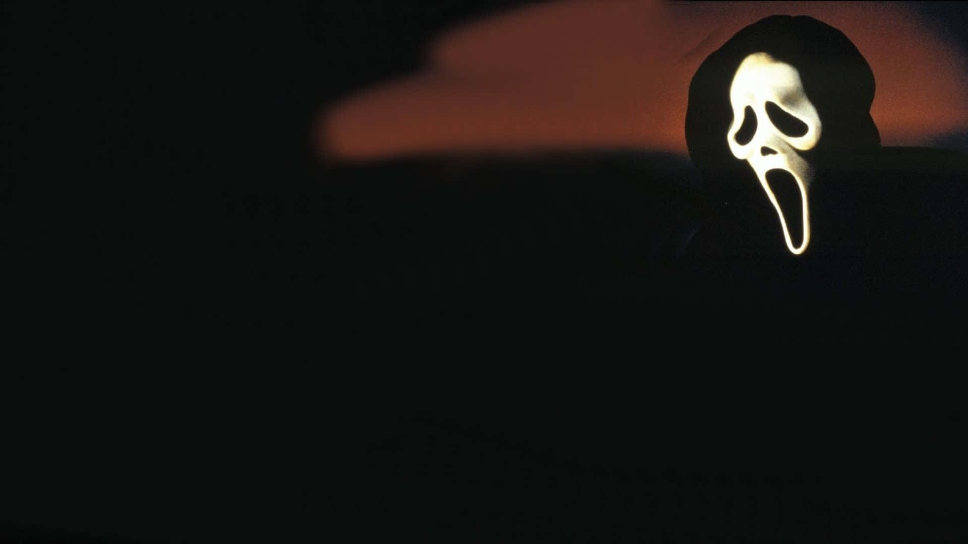 Scream Ghostface 桌布 壁紙 — 一個發光的白色尖叫面具從黑暗中浮現，背景是火紅的橙色日落天空。