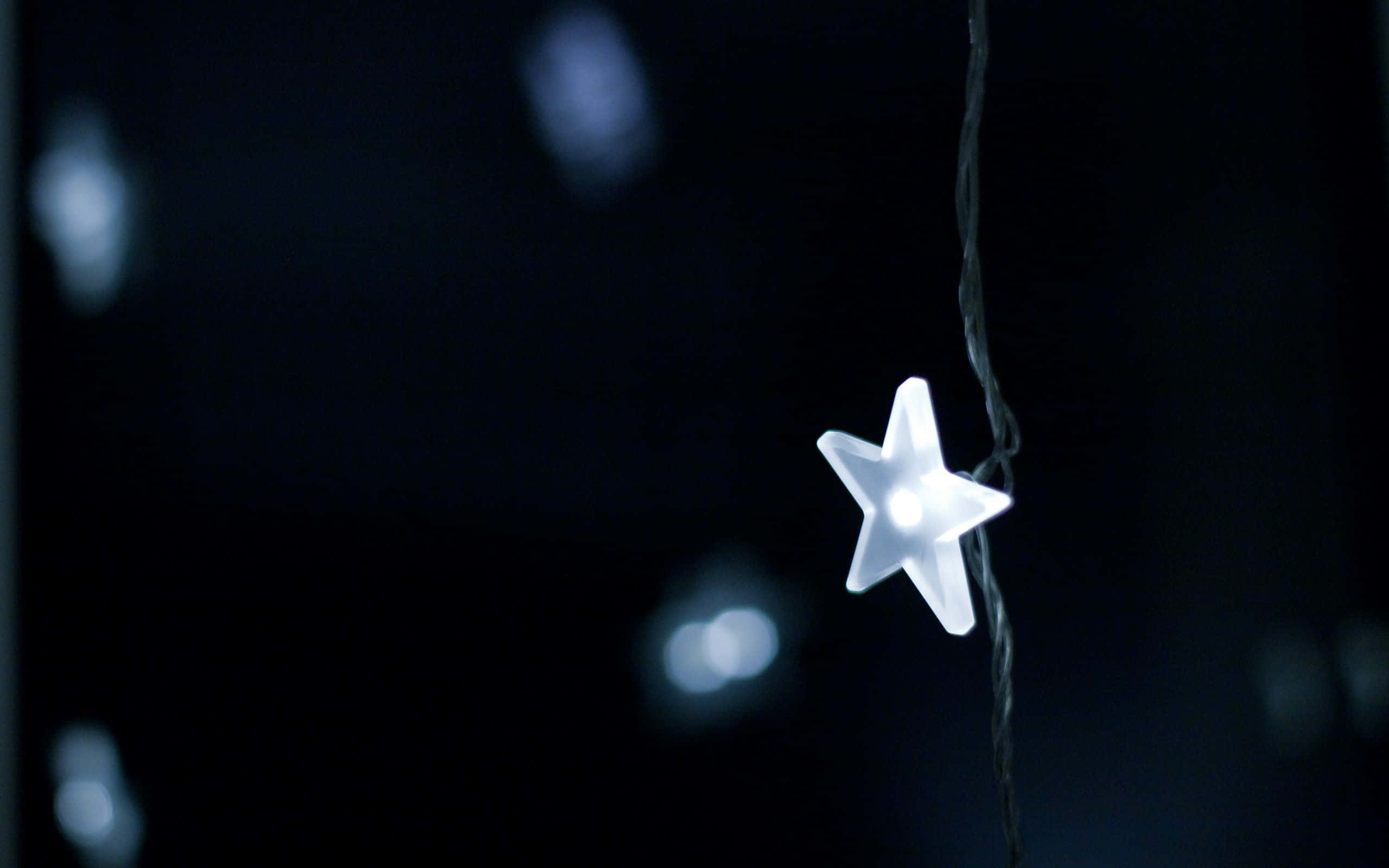 Cute Stars 桌布 壁紙 — 一個發光的白色星形燈懸掛在帶有模糊散景燈光的黑暗背景上。