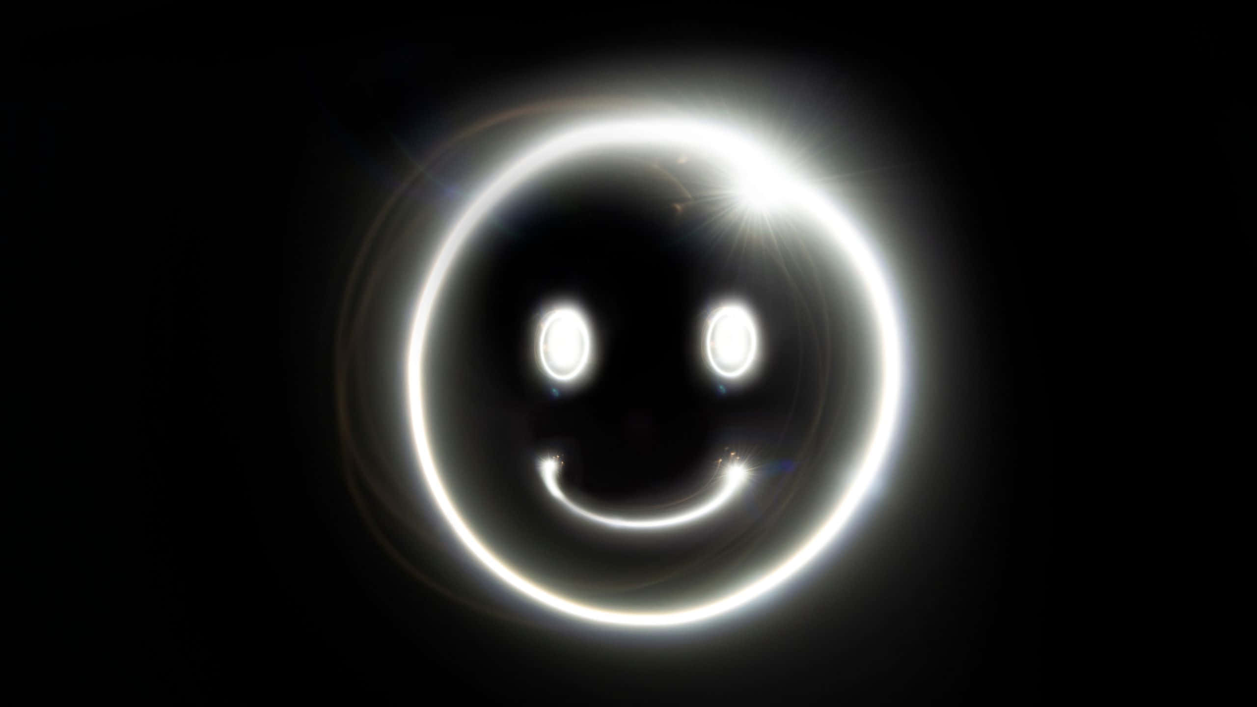 Smile Emoji 桌布 壁紙 — 一個發光的白色笑臉，帶有明亮的眼睛和彎曲的嘴巴，在純黑色背景上散發光芒。