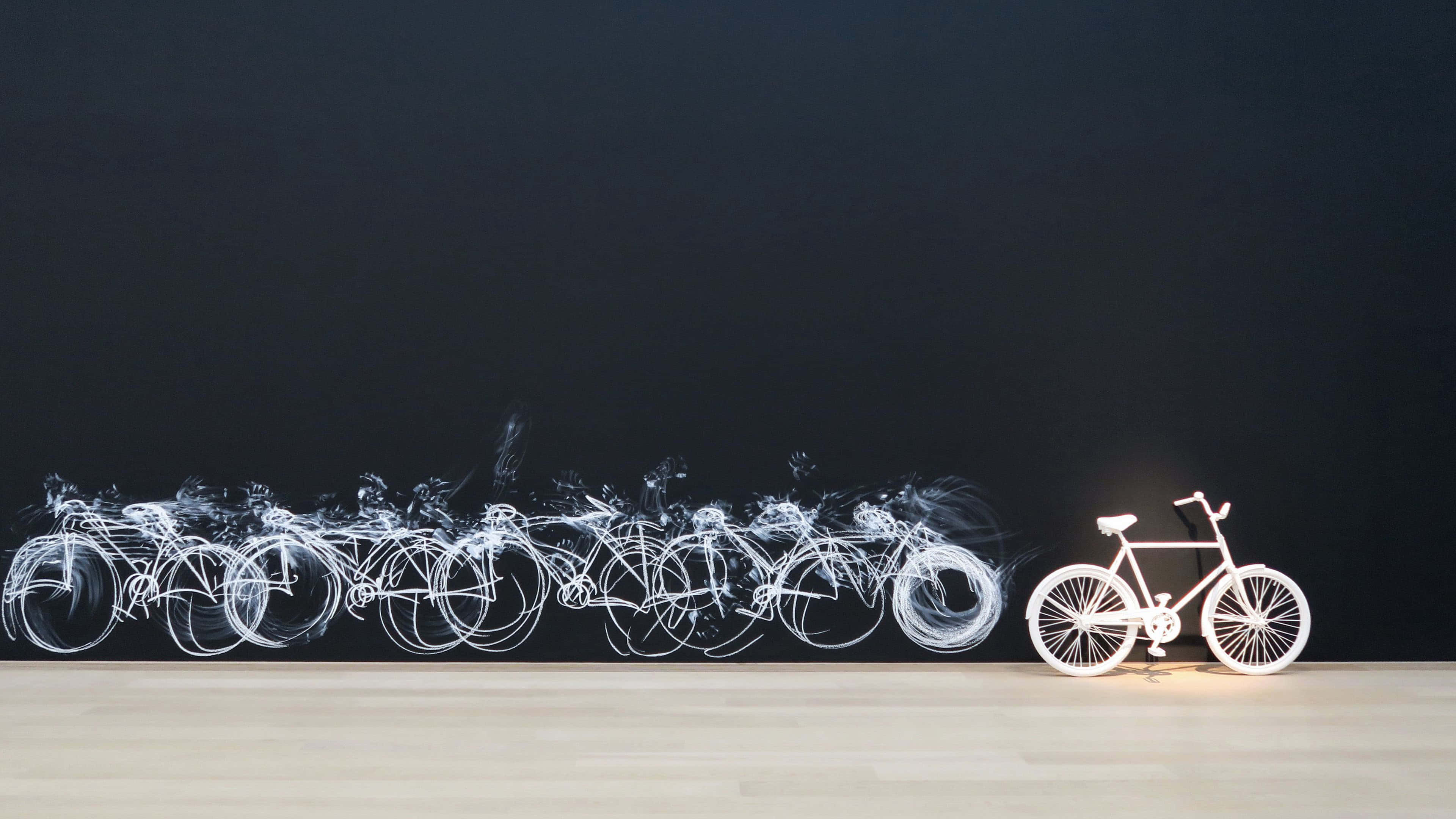 4K Bikes 桌布 壁紙 — 一個發光的白色自行車雕塑，旁邊是一條由光繪製的自行車輪廓軌跡，在一面黑暗的牆上。