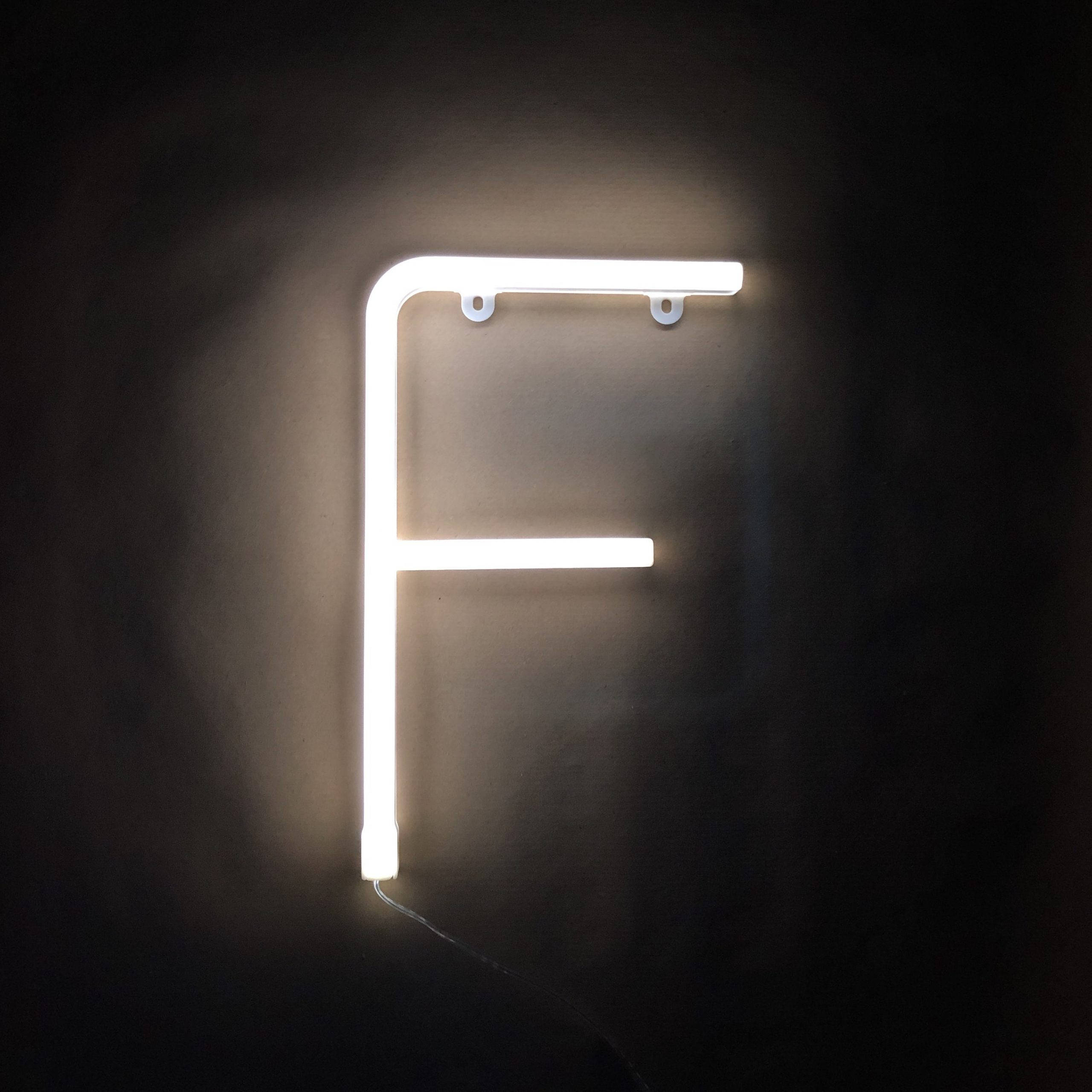 F 桌布 壁紙 — 一個發光的白色霓虹字母F安裝在深色牆壁上，在極簡環境中投射出柔和溫暖的光線。