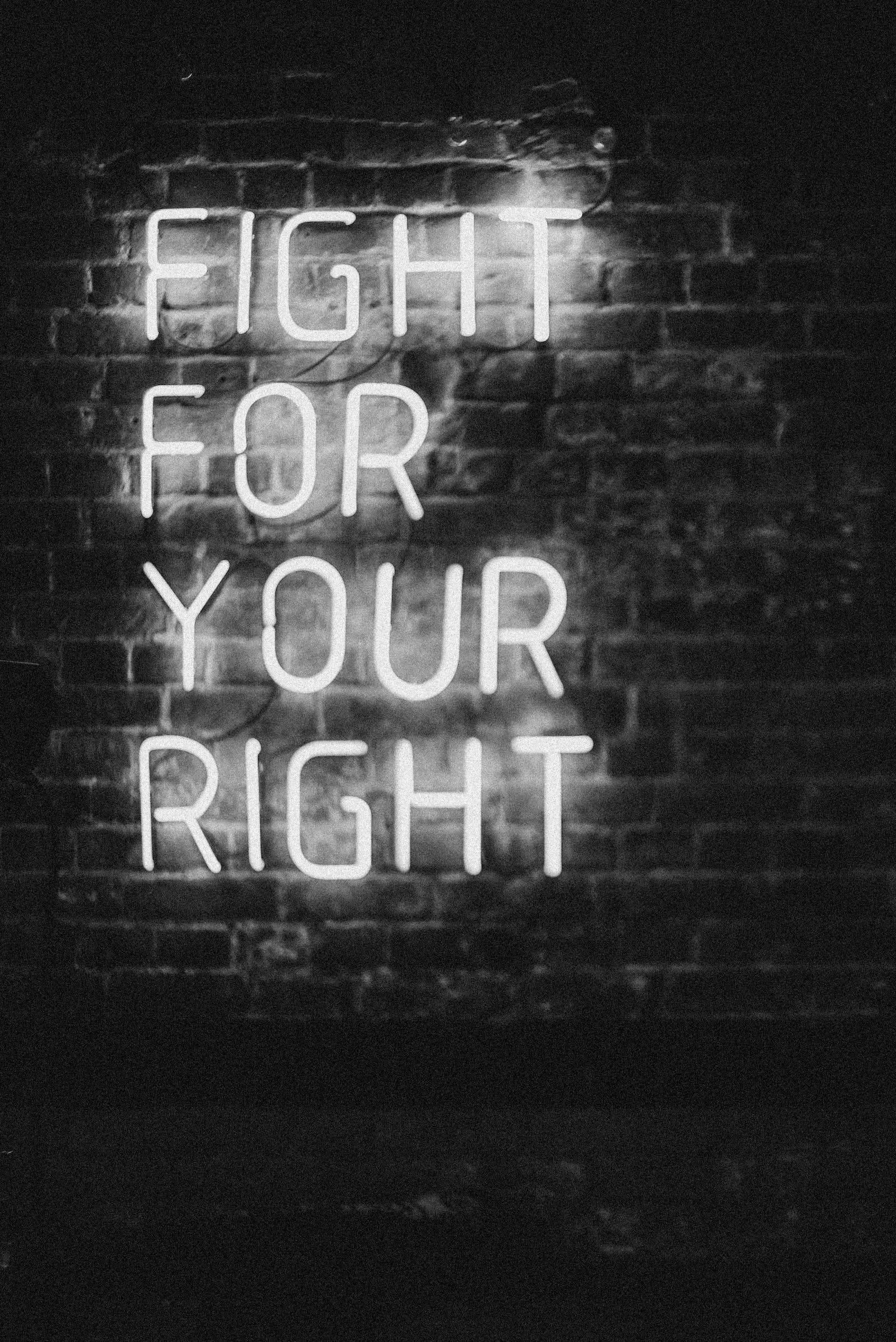 Motivation 桌布 壁紙 — 一個發光的白色霓虹燈牌，上面寫著 fight for your right，照亮了陰暗的磚牆，營造出憂鬱的城市夜景。