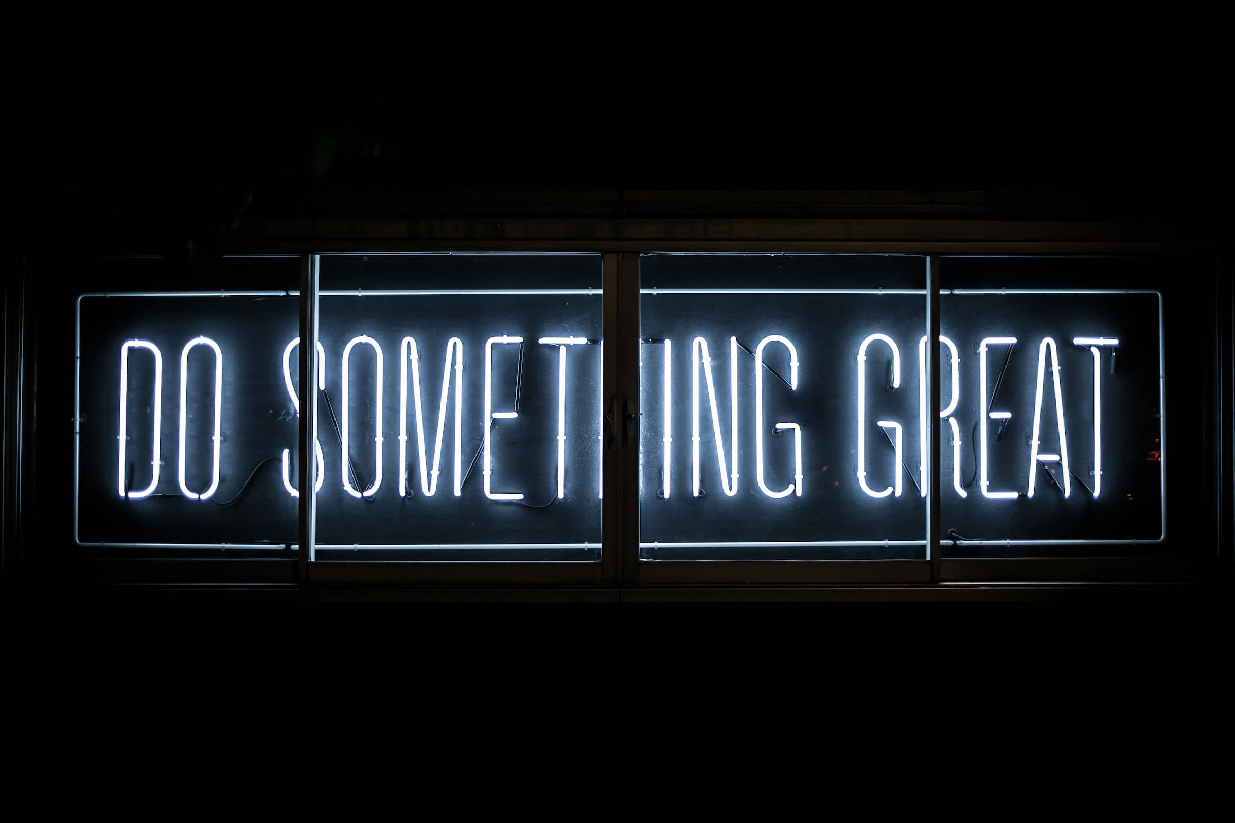 音樂 桌布 壁紙 — 一個發光的白色霓虹燈牌，上面寫著「DO SOMETHING GREAT」，在夜間照亮了黑暗的窗戶。
