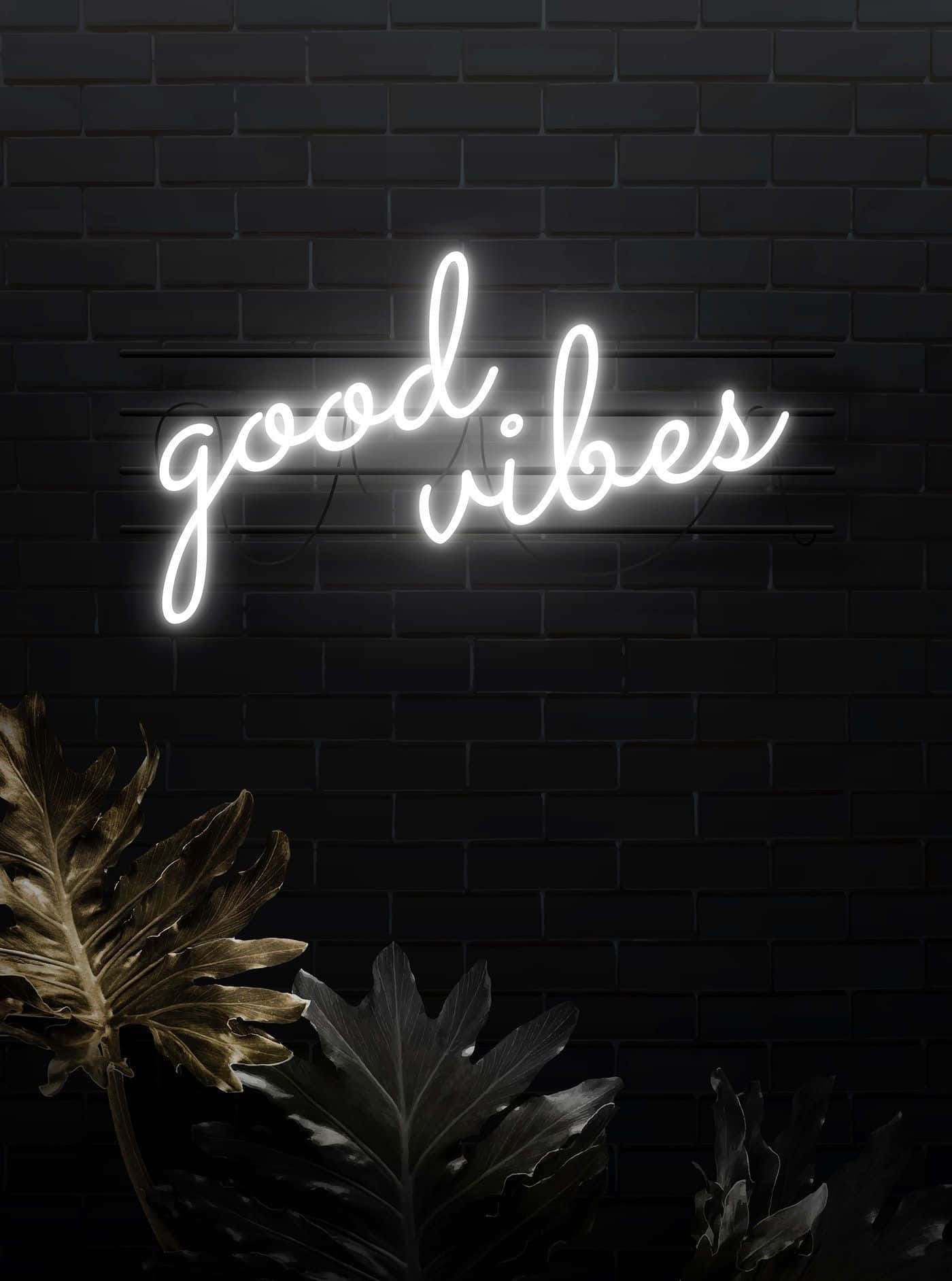 White Neon 桌布 壁紙 — 一個發光的白色霓虹燈牌，上面寫著 good vibes，照亮了旁邊有大型熱帶葉子的深色磚牆。