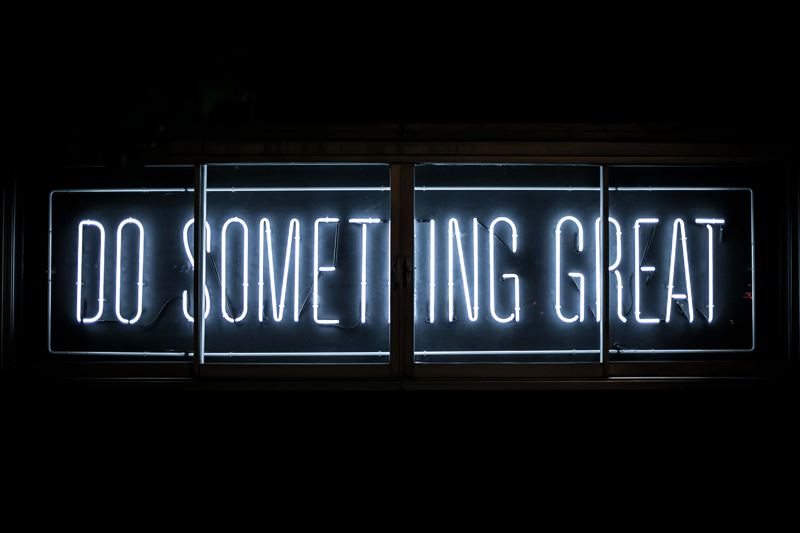 Light 桌布 壁紙 — 一個發光的白色霓虹燈牌，上面寫著「DO SOMETHING GREAT」，在夜晚照亮了黑暗的窗戶。